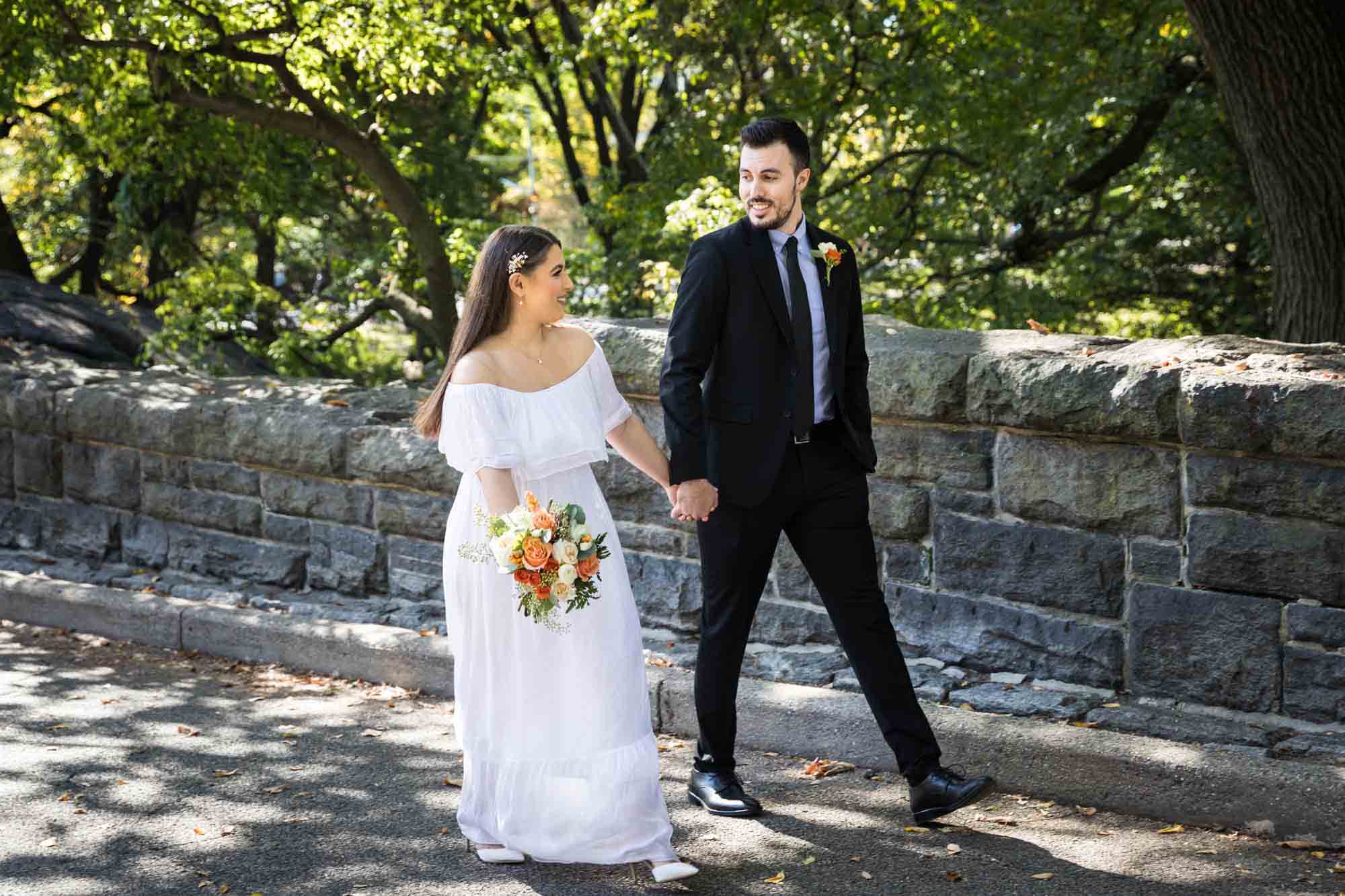 Bride and groom walking hand-in-hand in park Article on how to elope in Central Park by NYC wedding photojournalist, Kelly Williams. Includes photos from a real wedding near Bow Bridge.