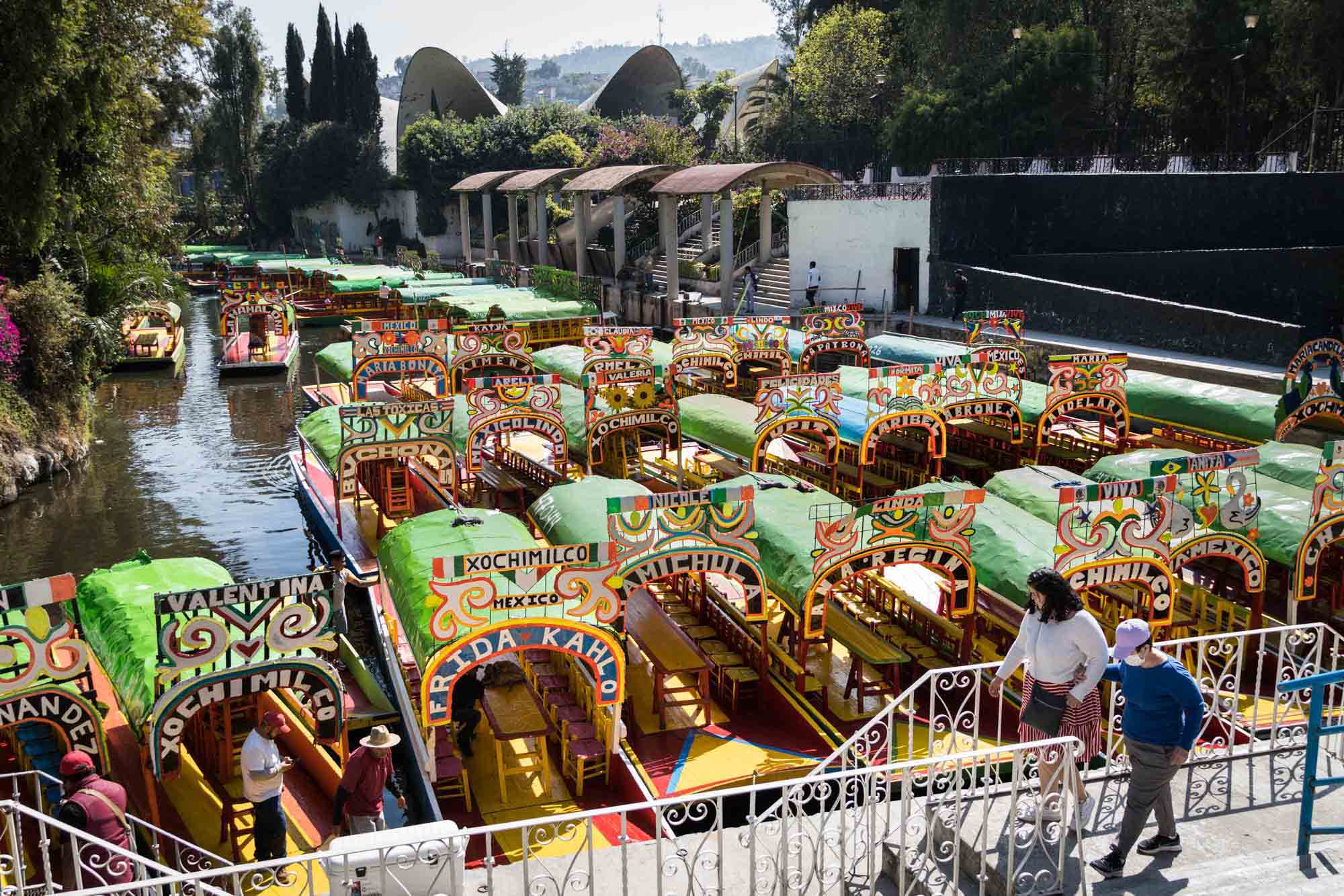 A couple walks past colorful boats in Xochimilco