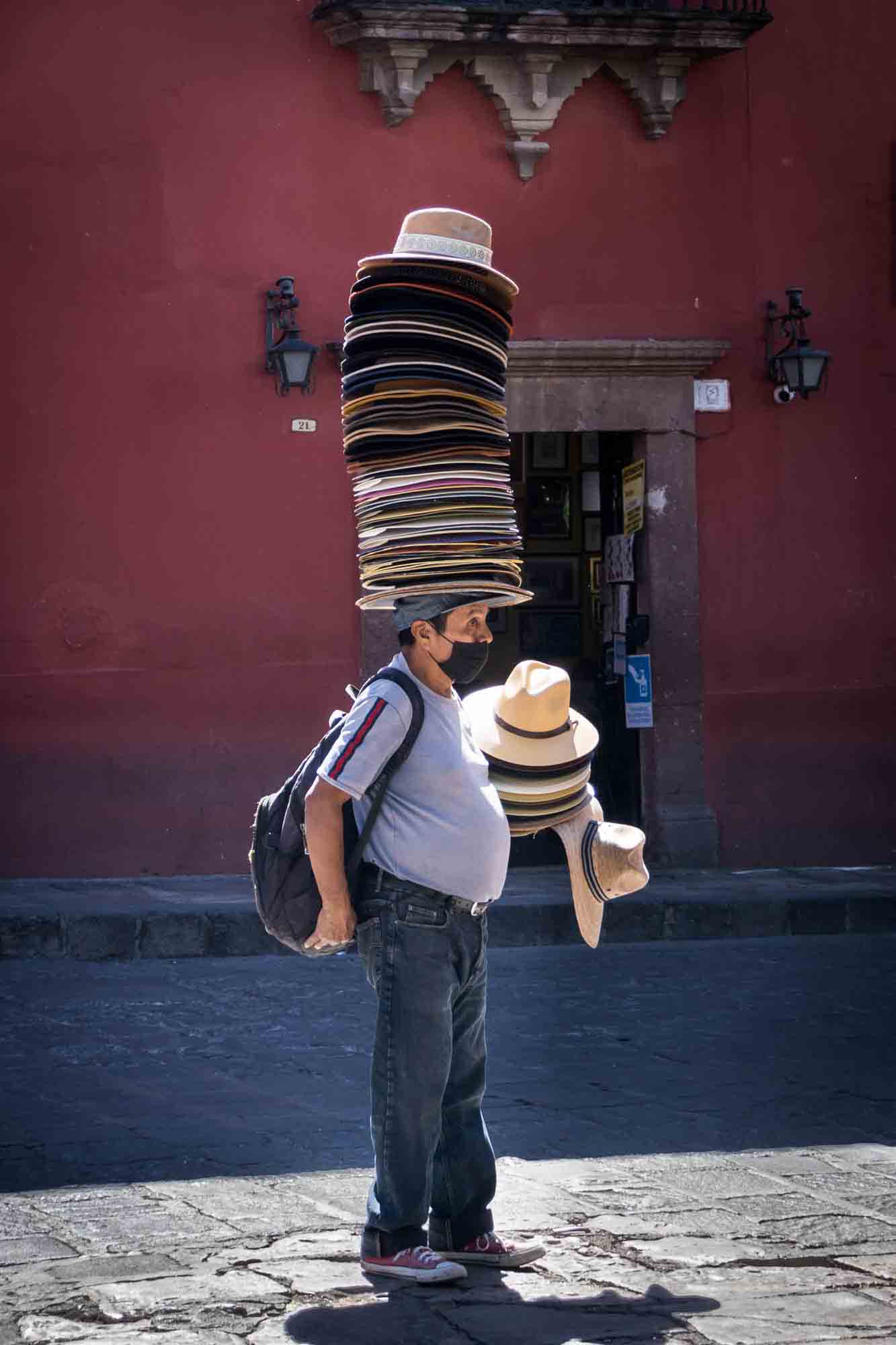 A man wears a stack of hats on his head in the streets of San Miguel de Allende