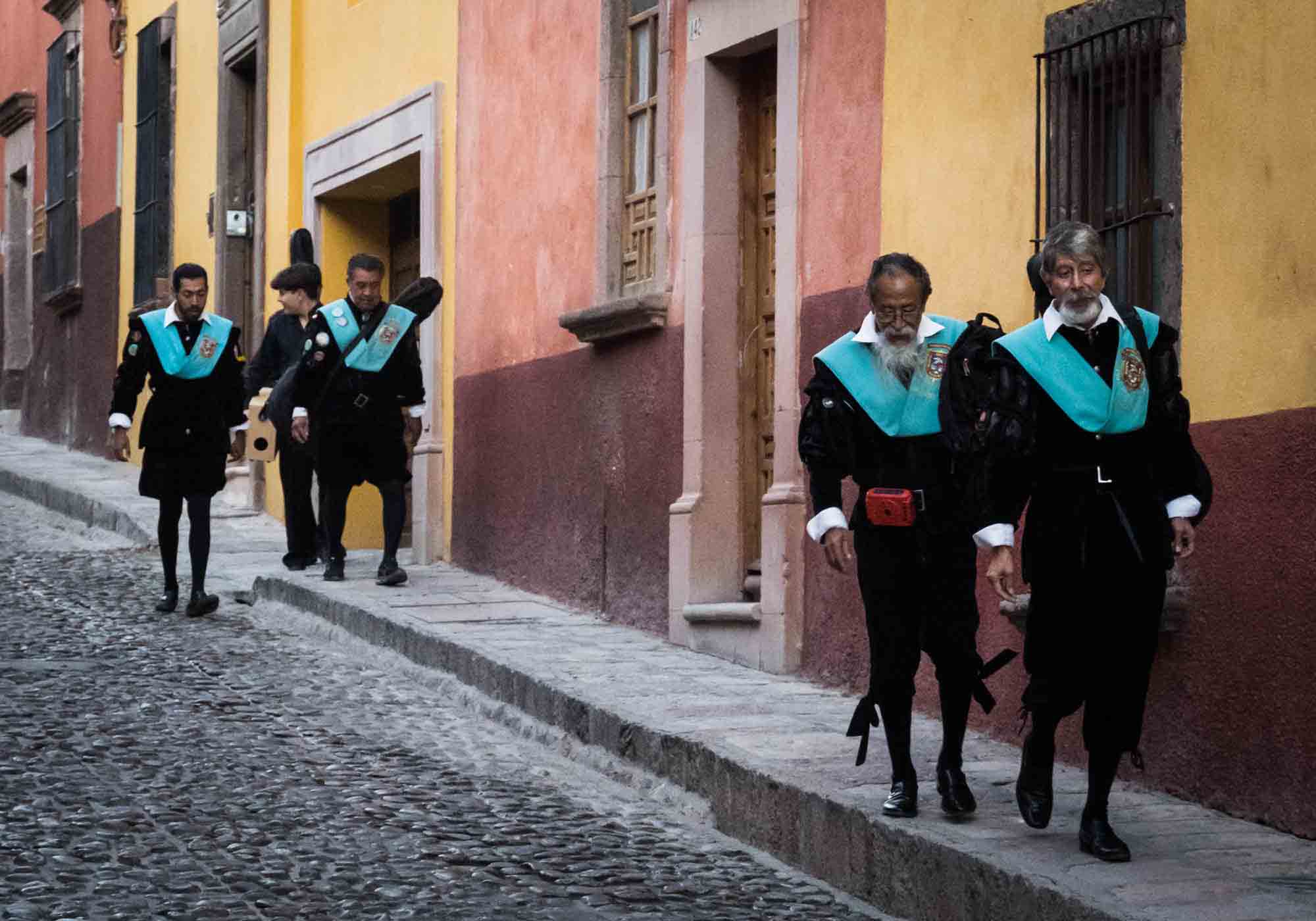 Men dressed in black and aqua traditional costumes walking down the street in San Miguel de Allende
