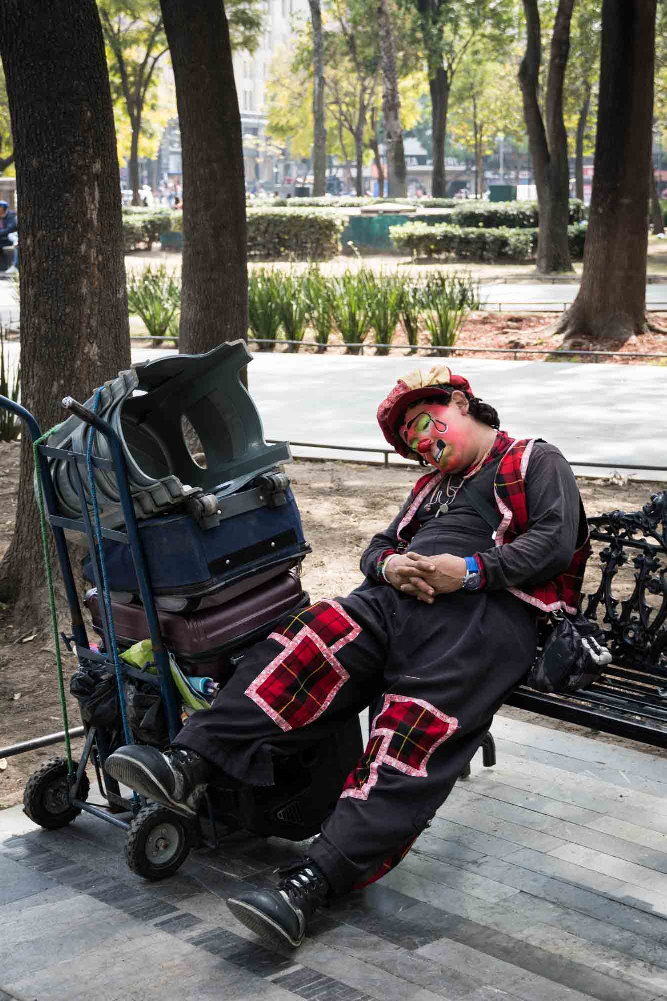 A clown takes a nap on a bench in Alameda Central Park in Mexico City
