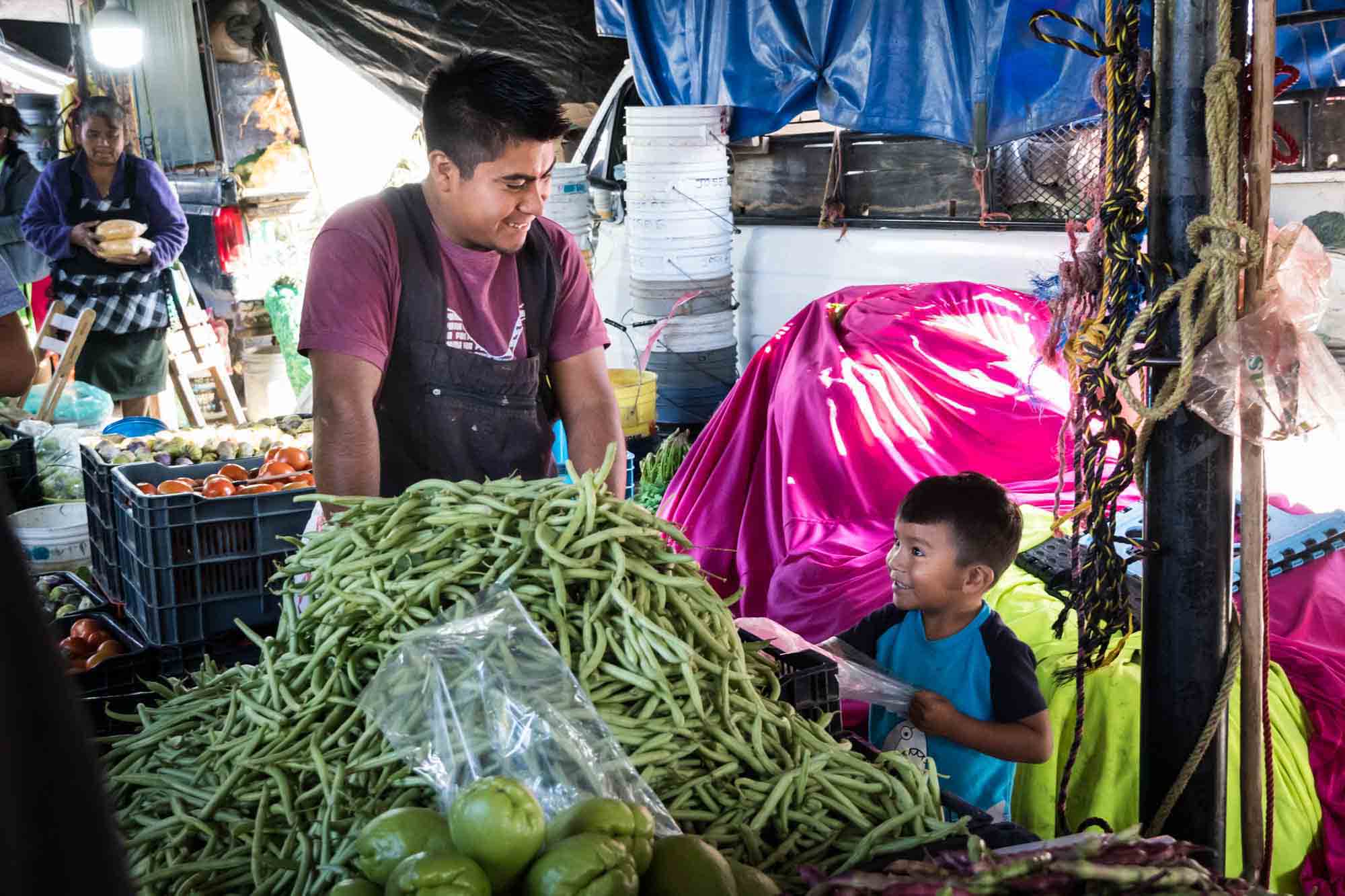 A father looking down at his son over a mountain of green beans in the Oaxaca market
