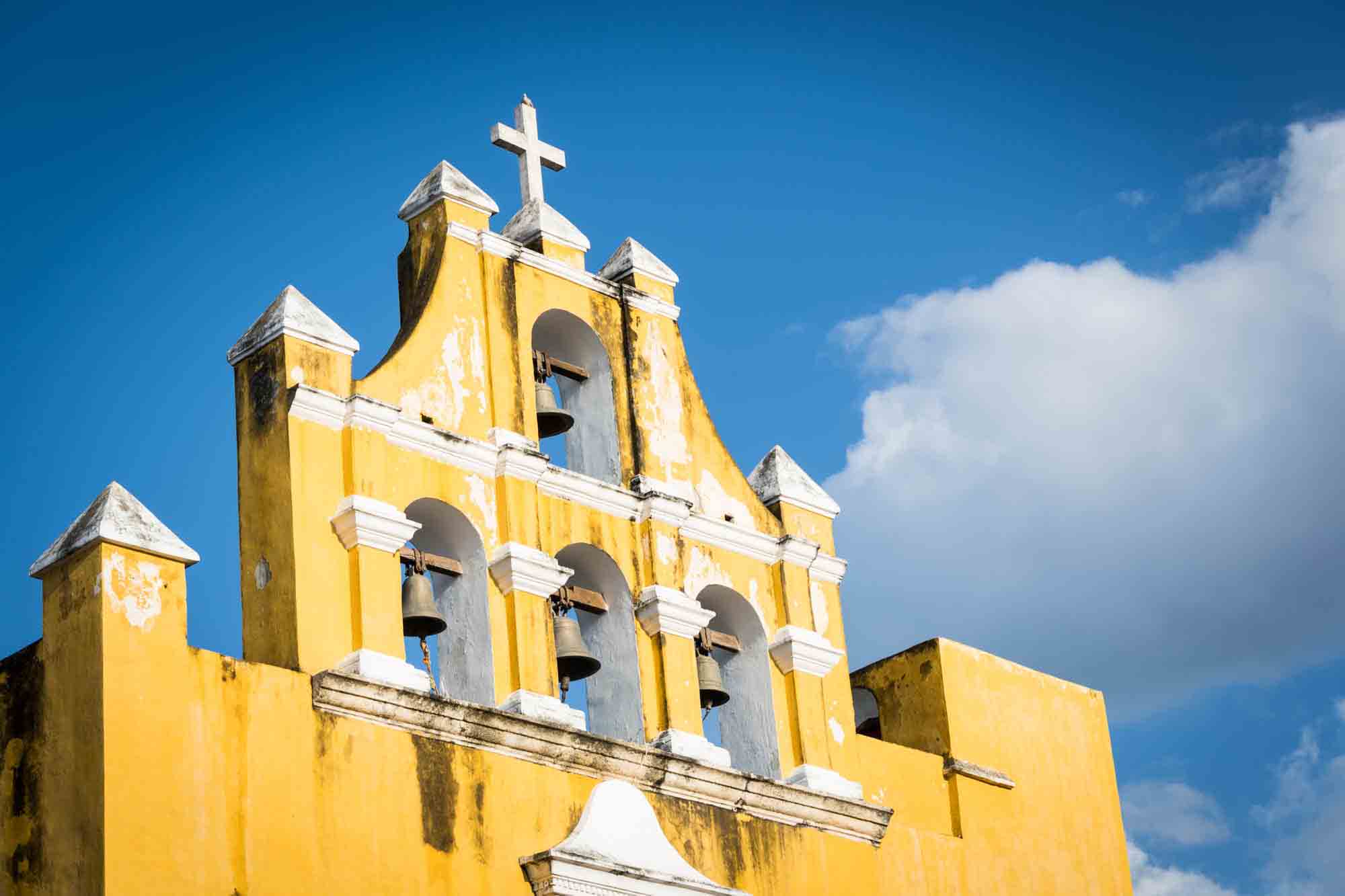 A church painted in yellow against a blue sky with clouds in Campeche