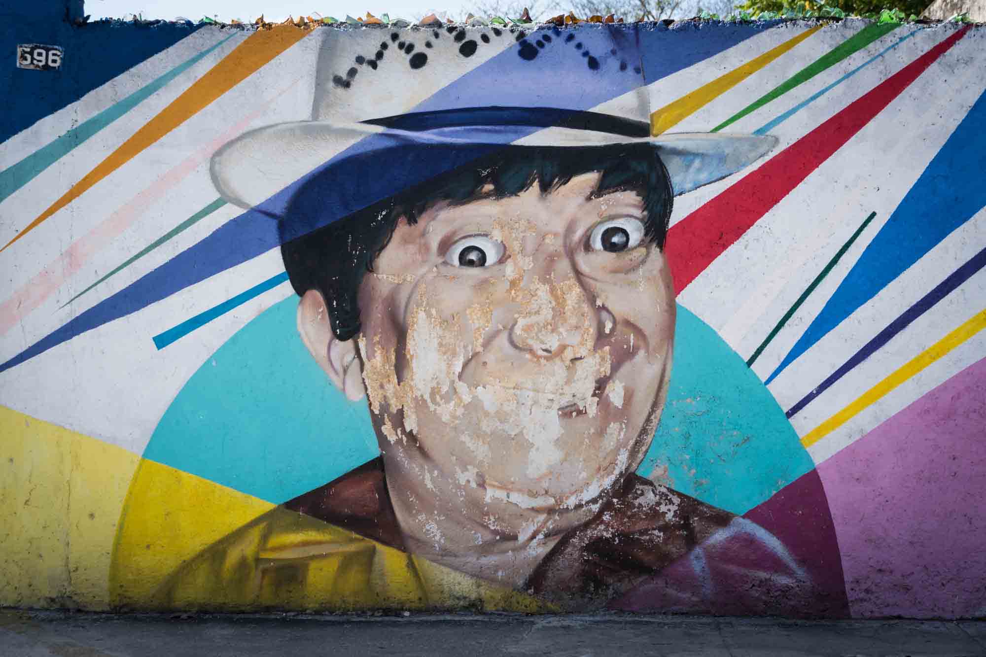 A colorful wall mural of a man wearing a hat on the streets of Merida