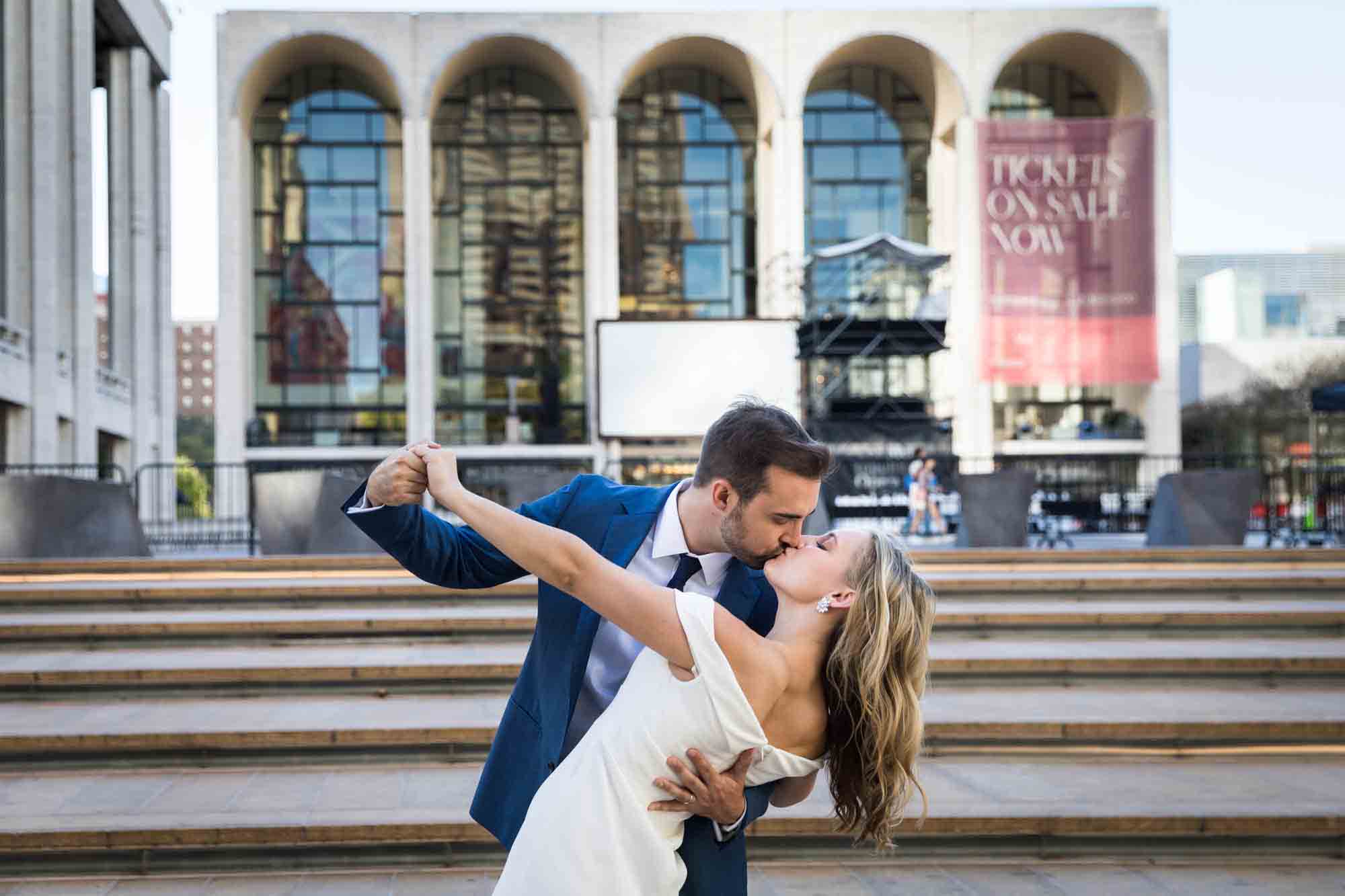 Groom kissing bride during dip in front of steps of Lincoln Plaza in NYC