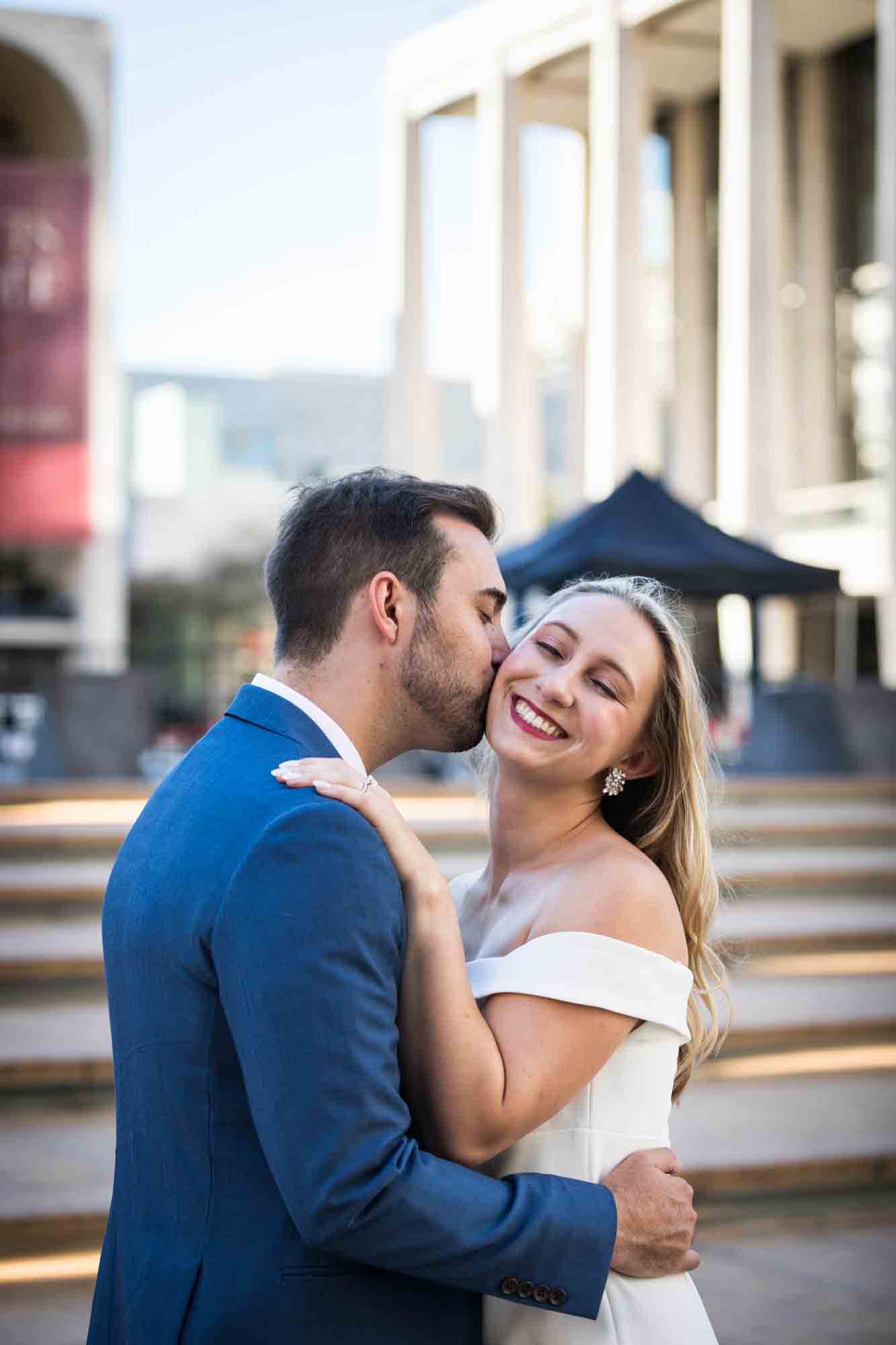Groom kissing bride on the cheek in front of Lincoln Plaza