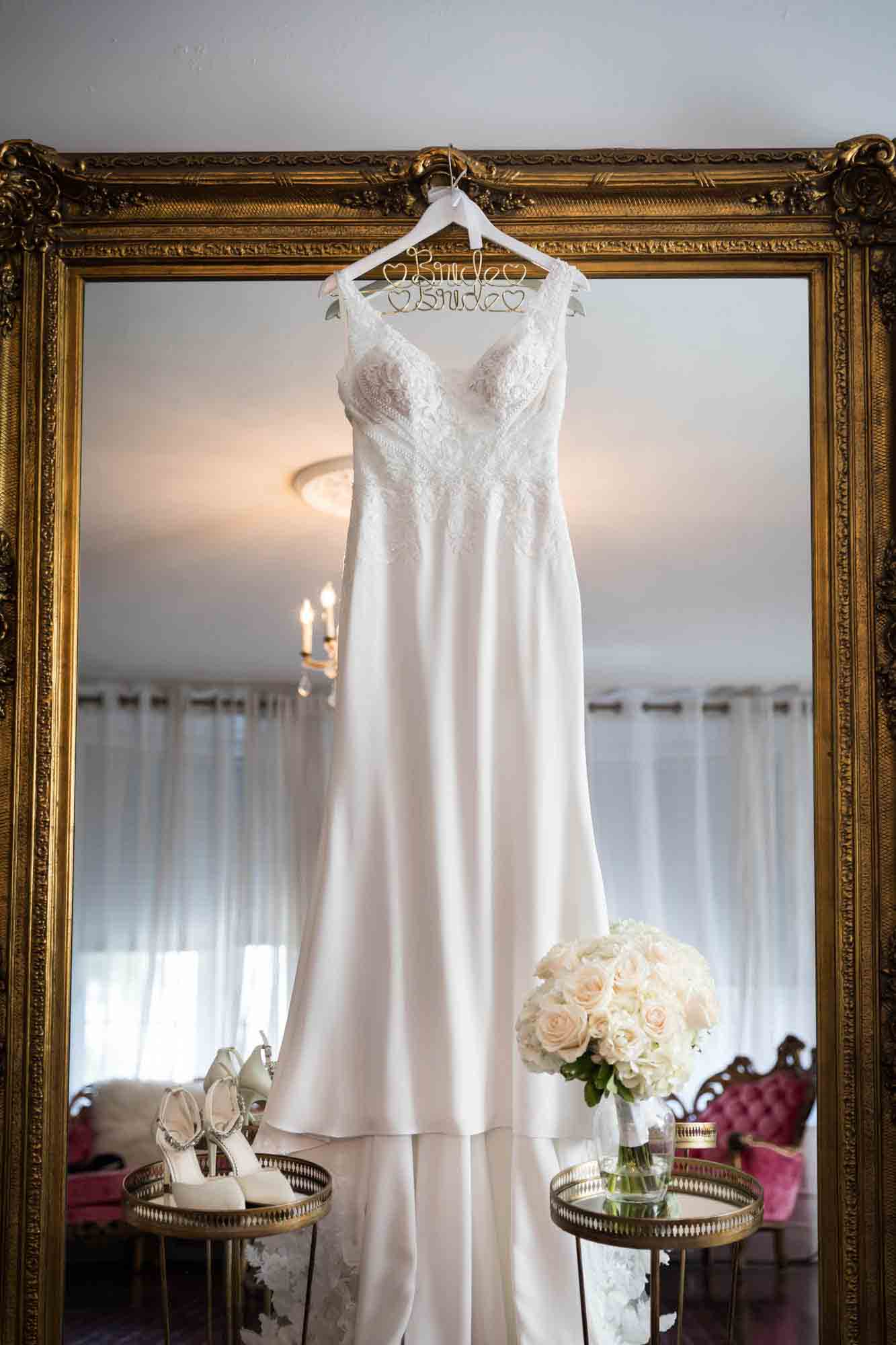 Wedding dress, white high heels, and white flower bouquet in front of vintage mirror in Briarcliff Manor bridal suite