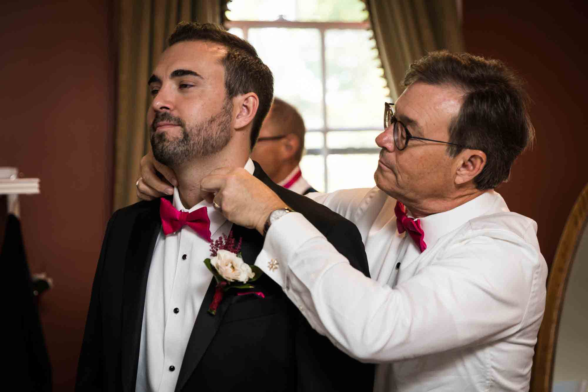 Father adjusting collar of groom wearing pink bow tie at a Briarcliff Manor wedding