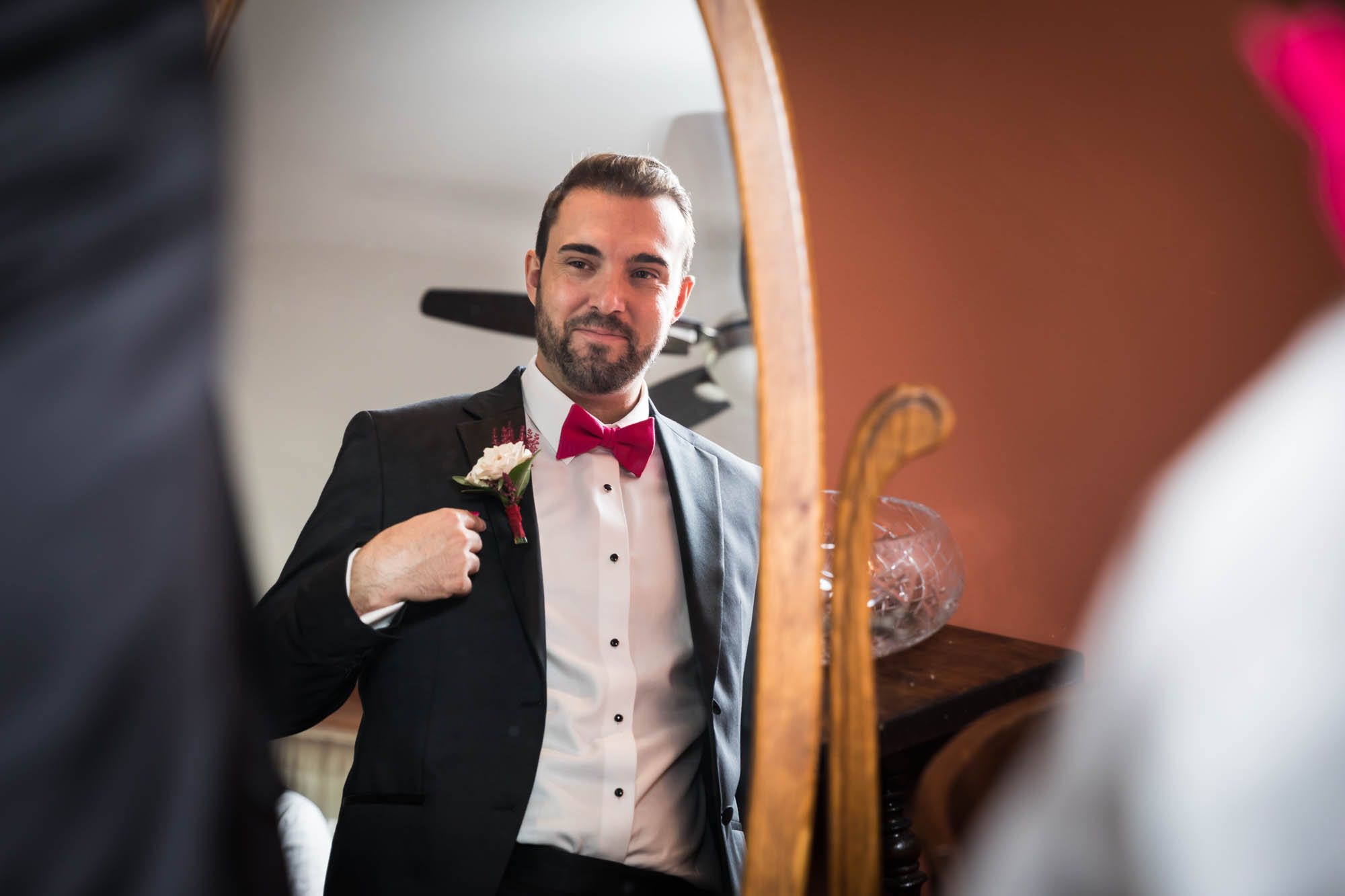 Groom touching jacket and looking at himself in the mirror at a Briarcliff Manor wedding