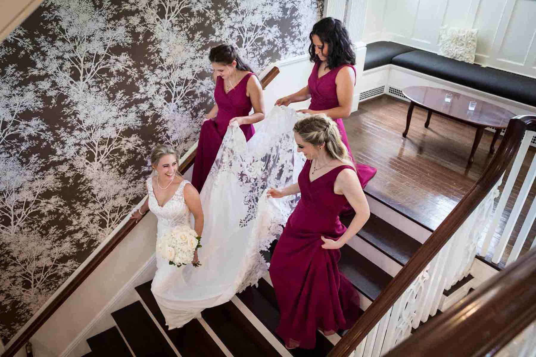 Bride and three bridesmaids wearing dark pink dresses walking down staircase at a Briarcliff Manor wedding