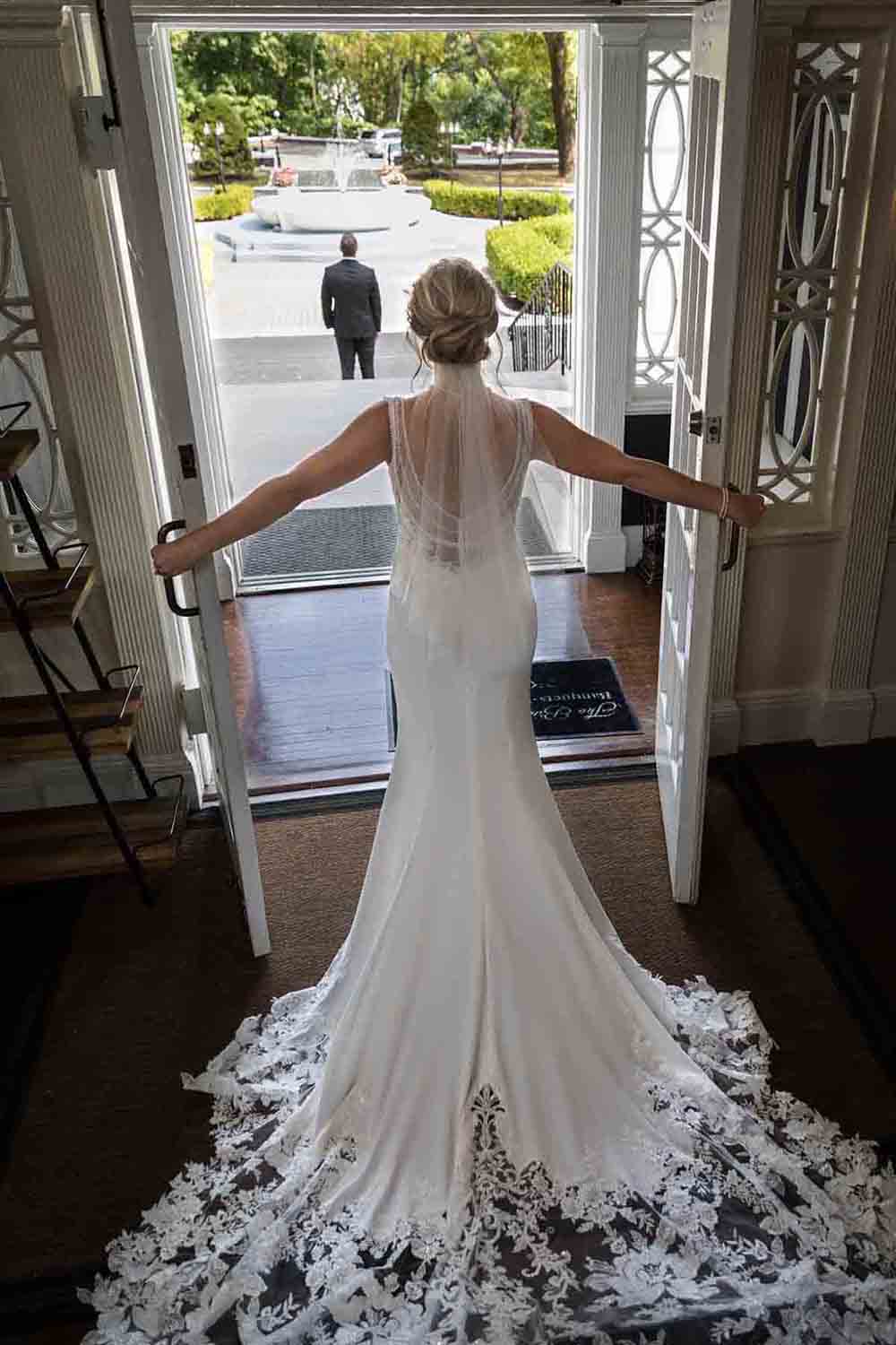 Bride wearing white dress with long train holding French doors open at a Briarcliff Manor wedding