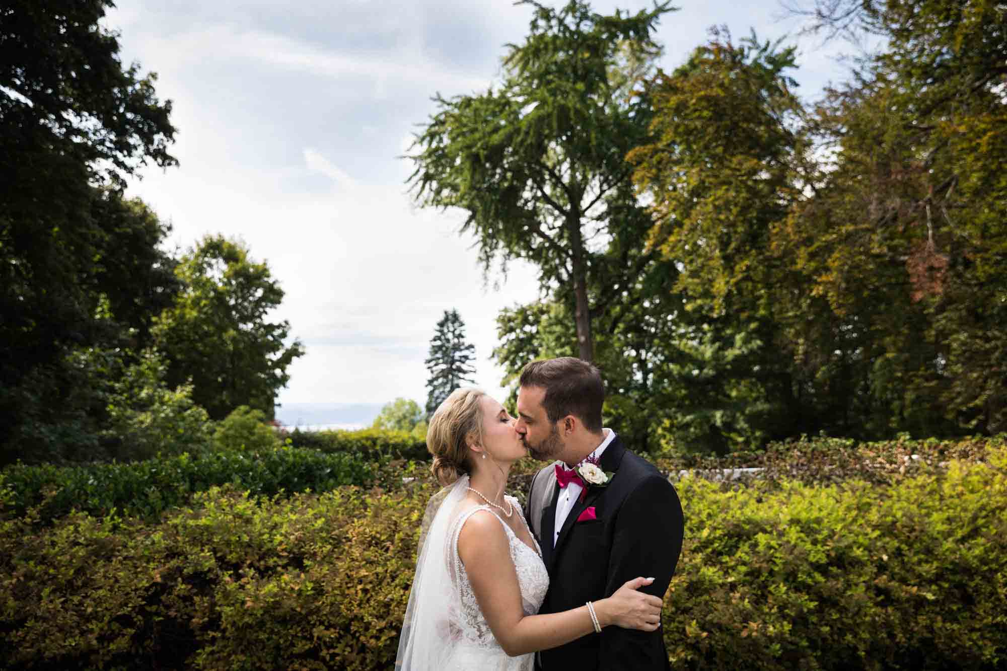 Bride and groom kissing in front of hedge and trees at a Briarcliff Manor wedding