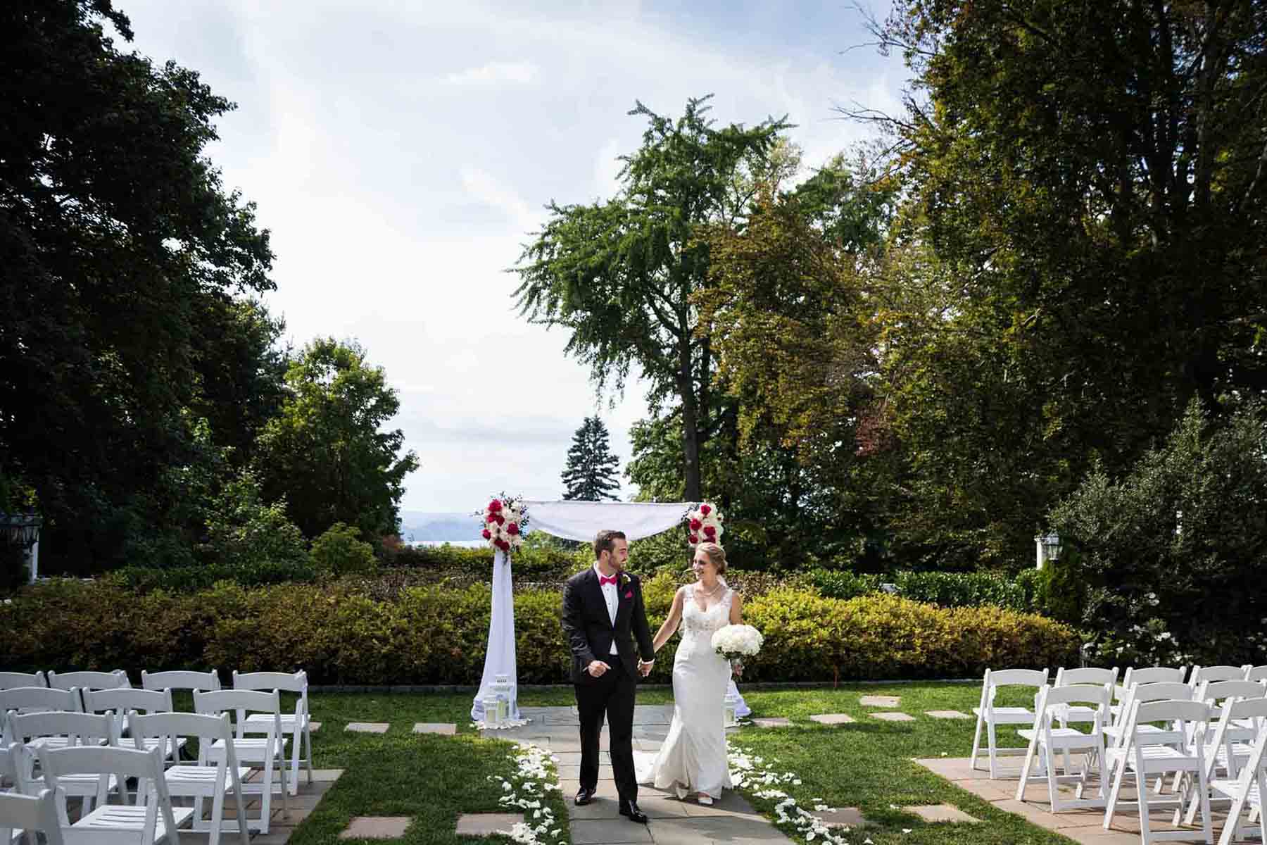 Bride and groom walking up aisle between white chairs at a Briarcliff Manor wedding