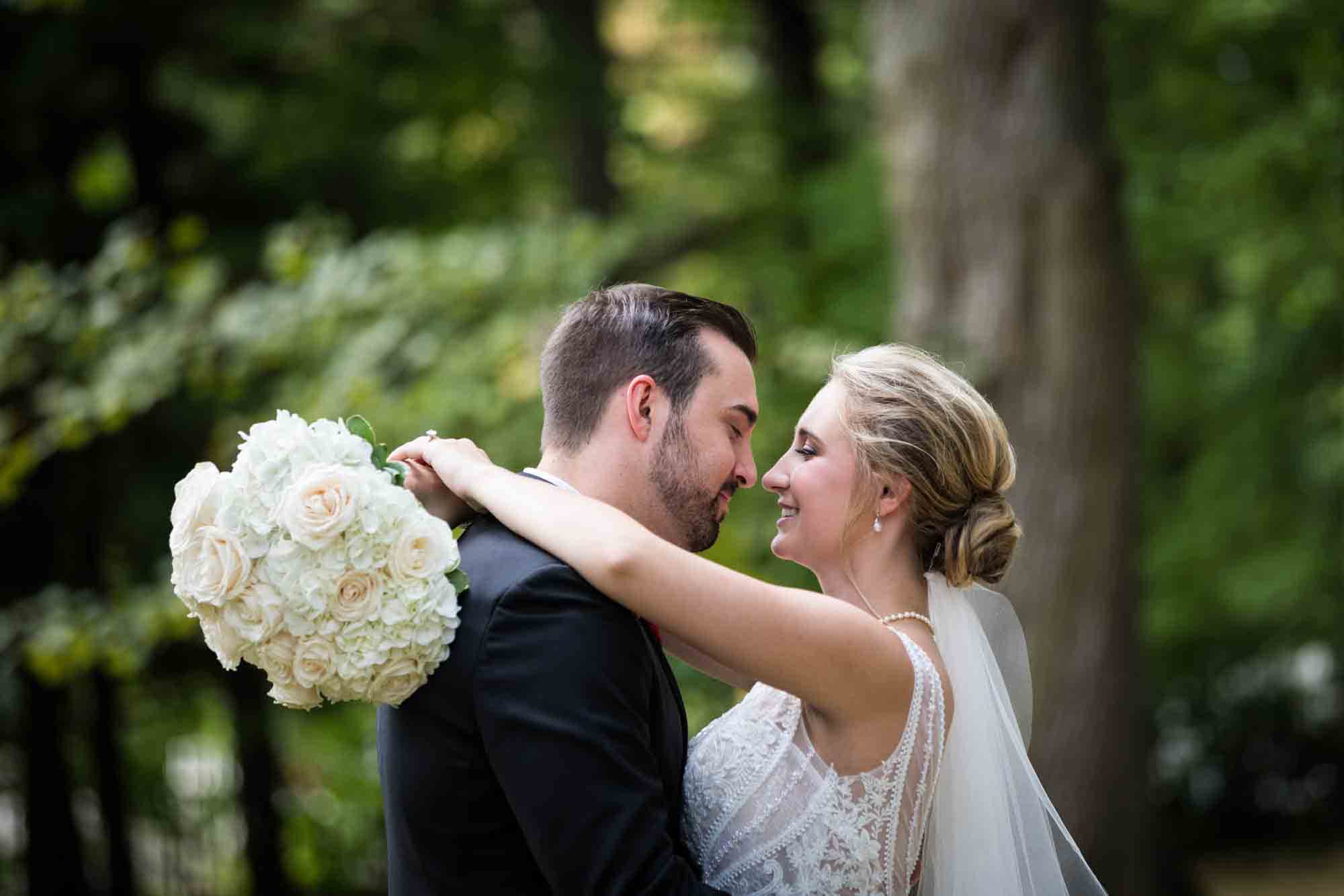Bride hugging groom with arms around his neck holding white flower bouquet at a Briarcliff Manor wedding