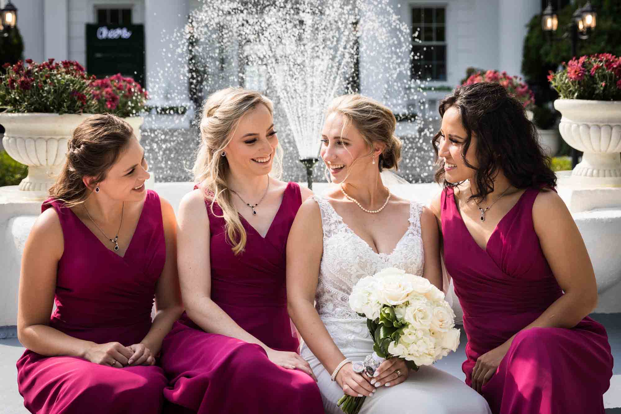 Bride and bridesmaids smiling at each other in front of fountain at a Briarcliff Manor wedding