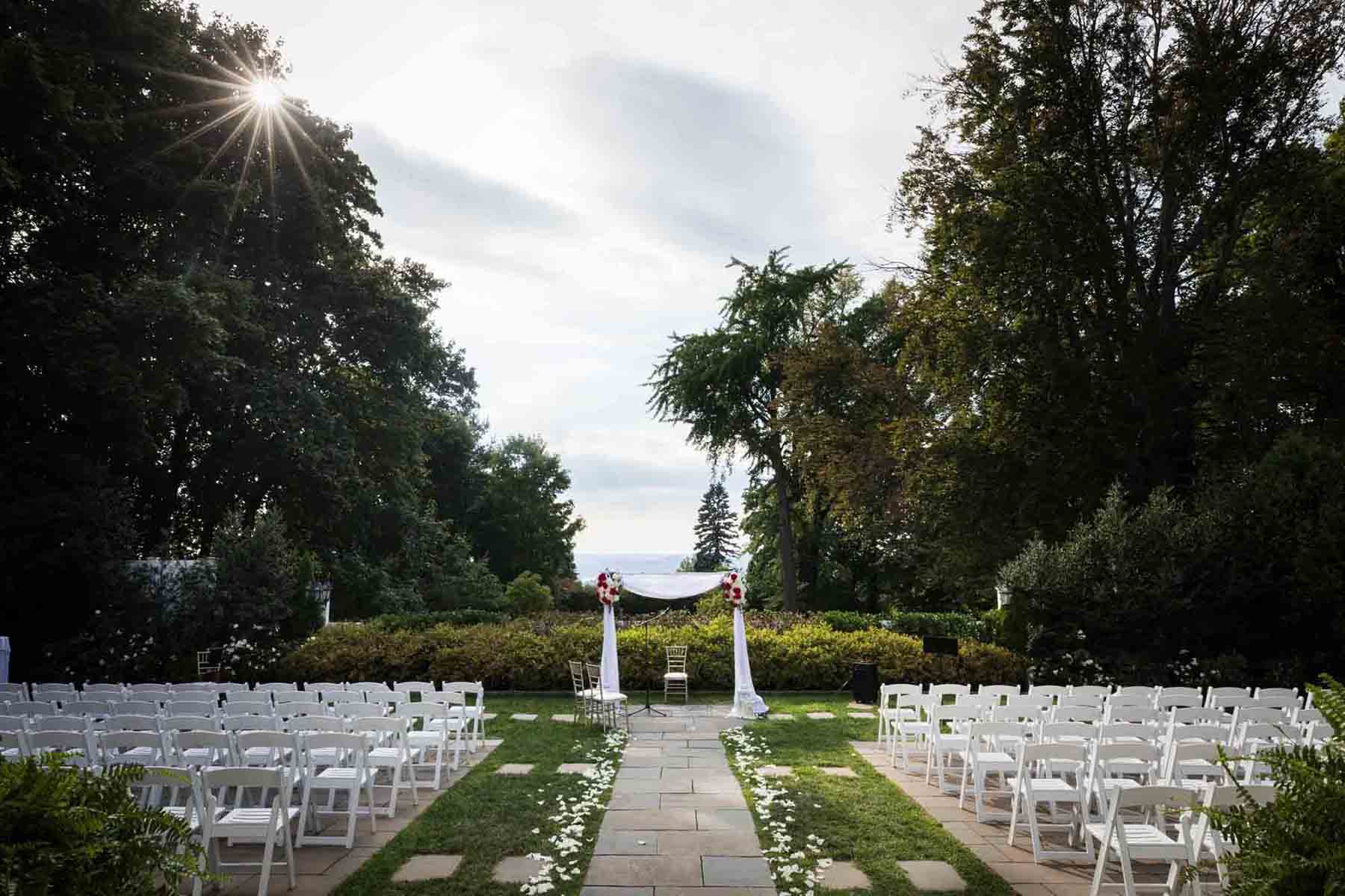 Outdoor ceremony space with rows of white chairs and white arch in center aisle at a Briarcliff Manor wedding