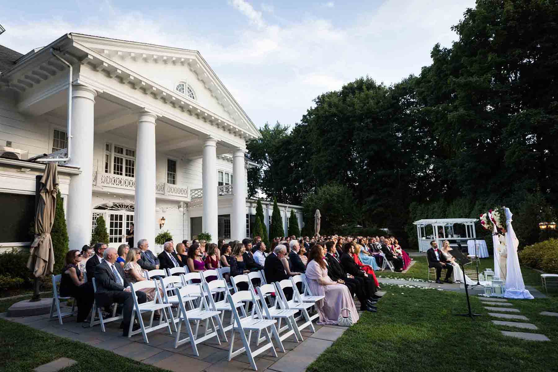 Wedding ceremony outdoors in front of historical white house with columns at a Briarcliff Manor wedding