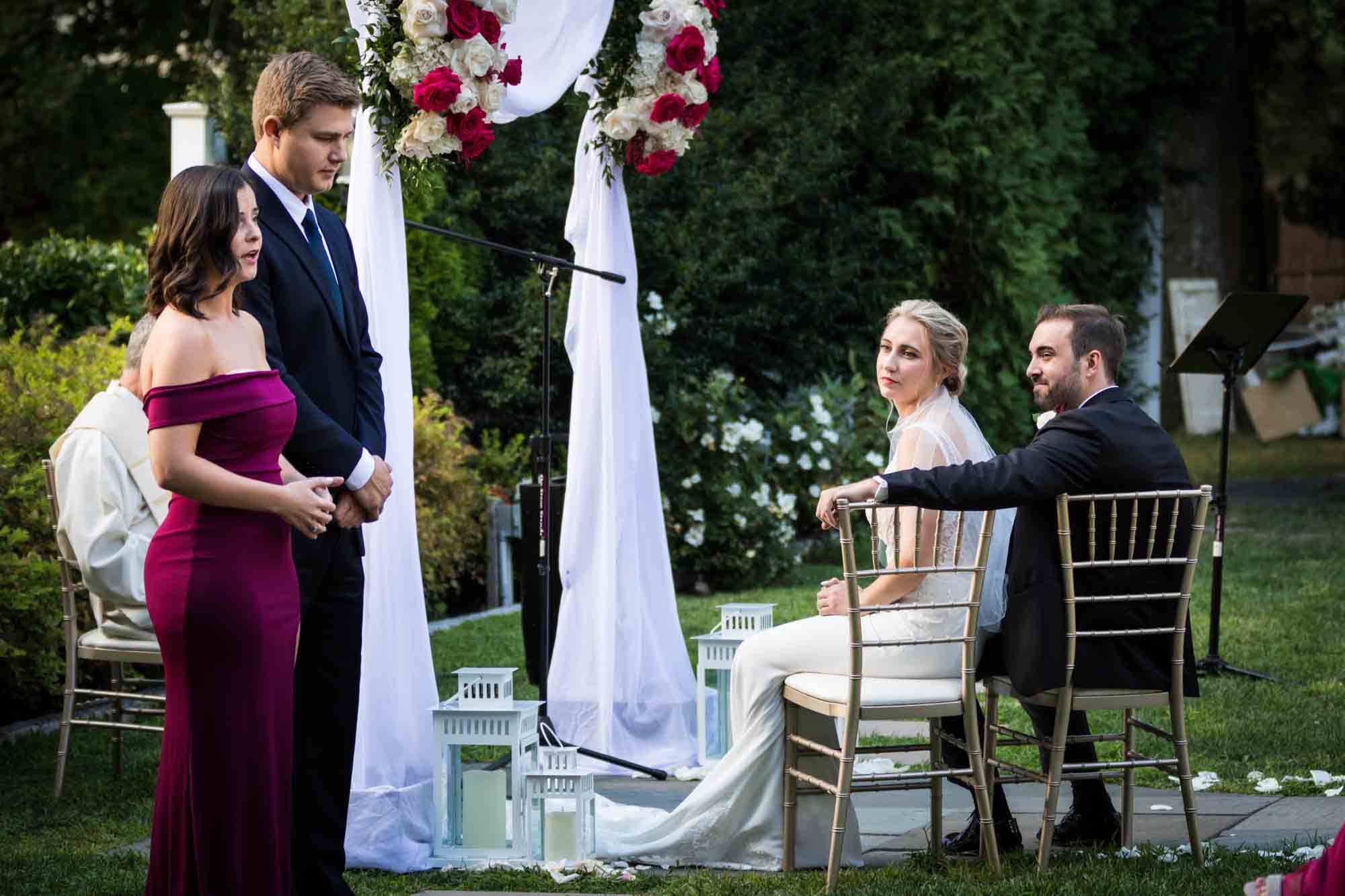 Seated bride and groom watching couple sing during outdoor ceremony at a Briarcliff Manor wedding
