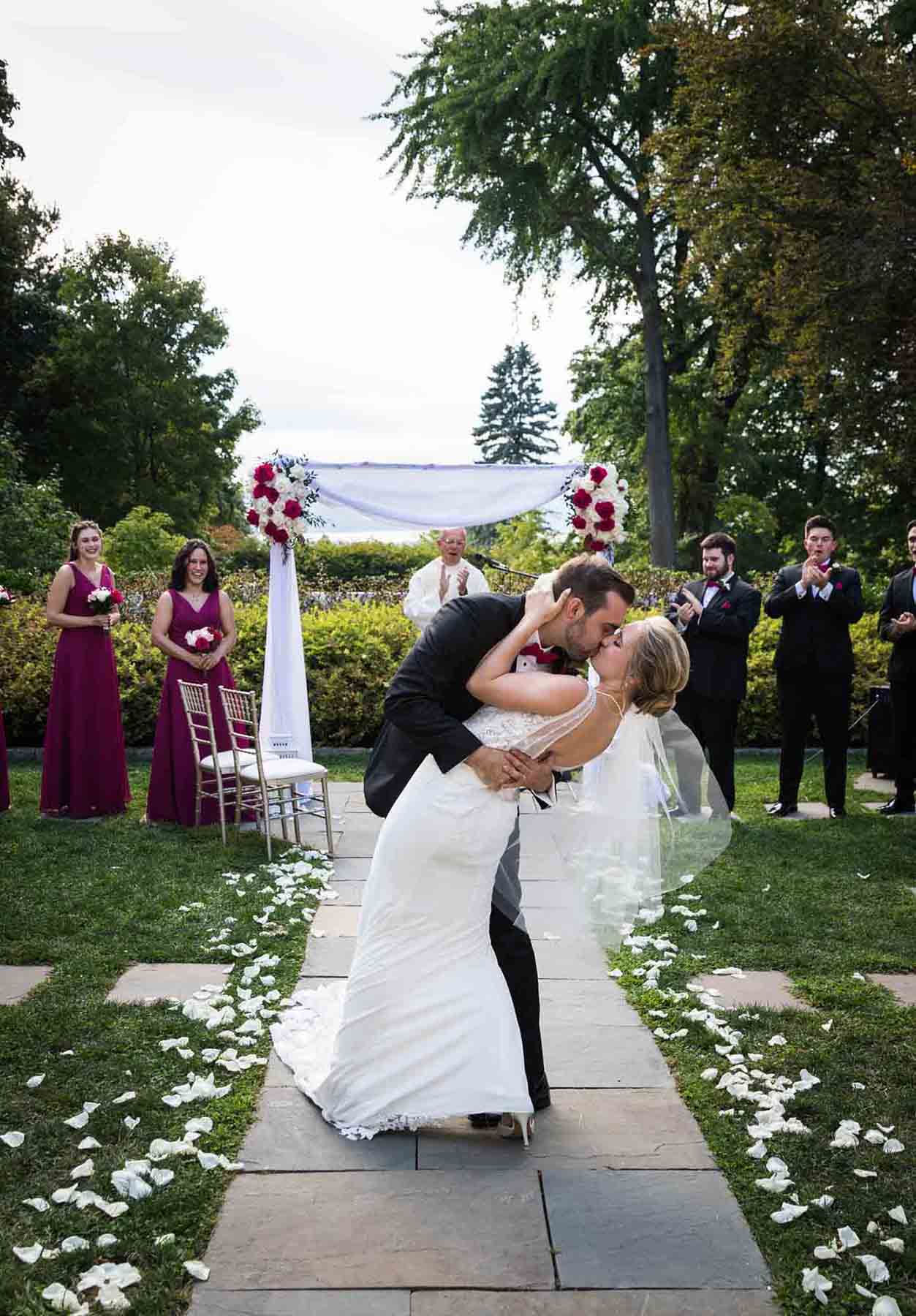 Bride and groom kissing in dramatic dip in middle of aisle after ceremony at a Briarcliff Manor wedding