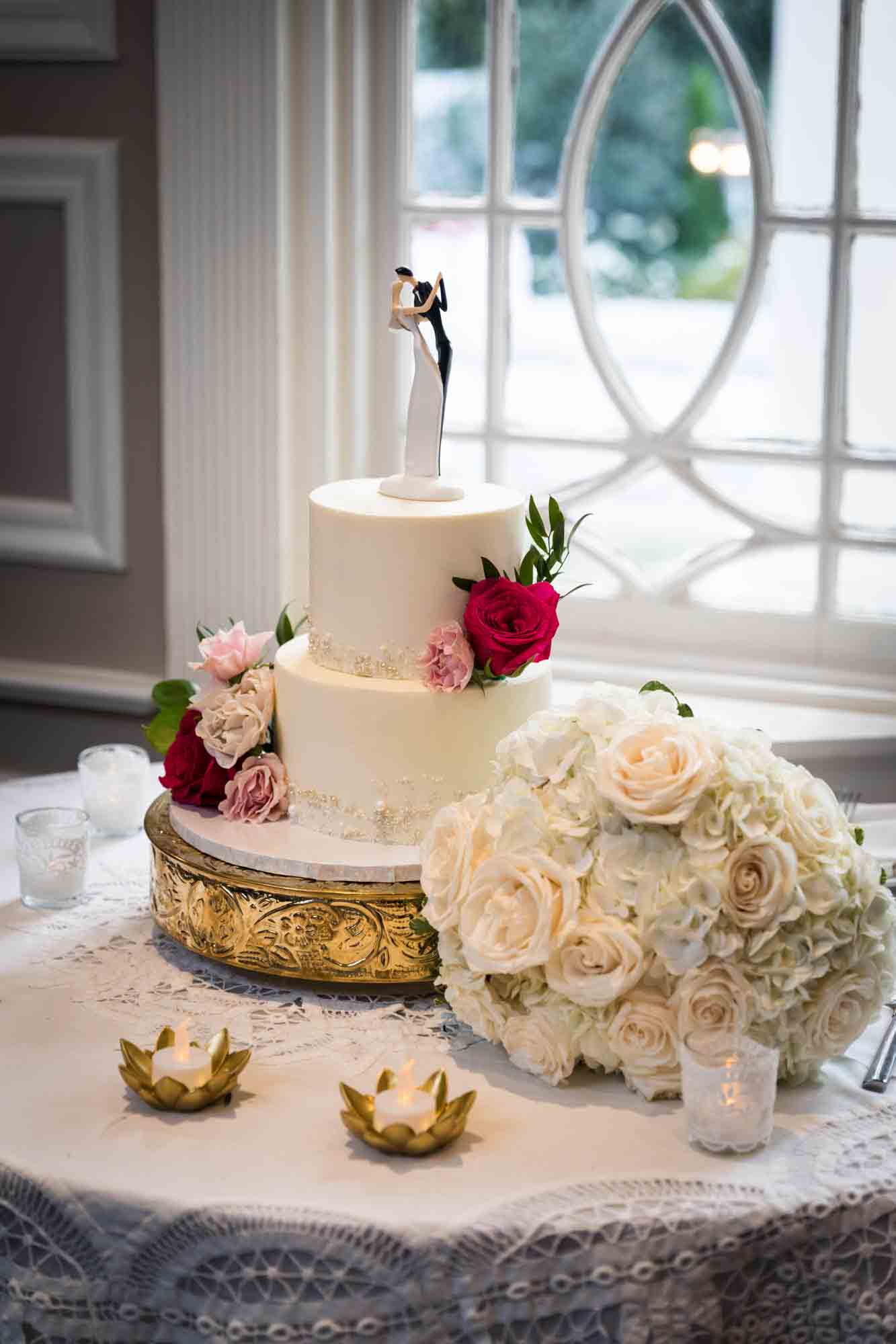 Two layer wedding cake with white flower bouquet on table in front of window at a Briarcliff Manor wedding