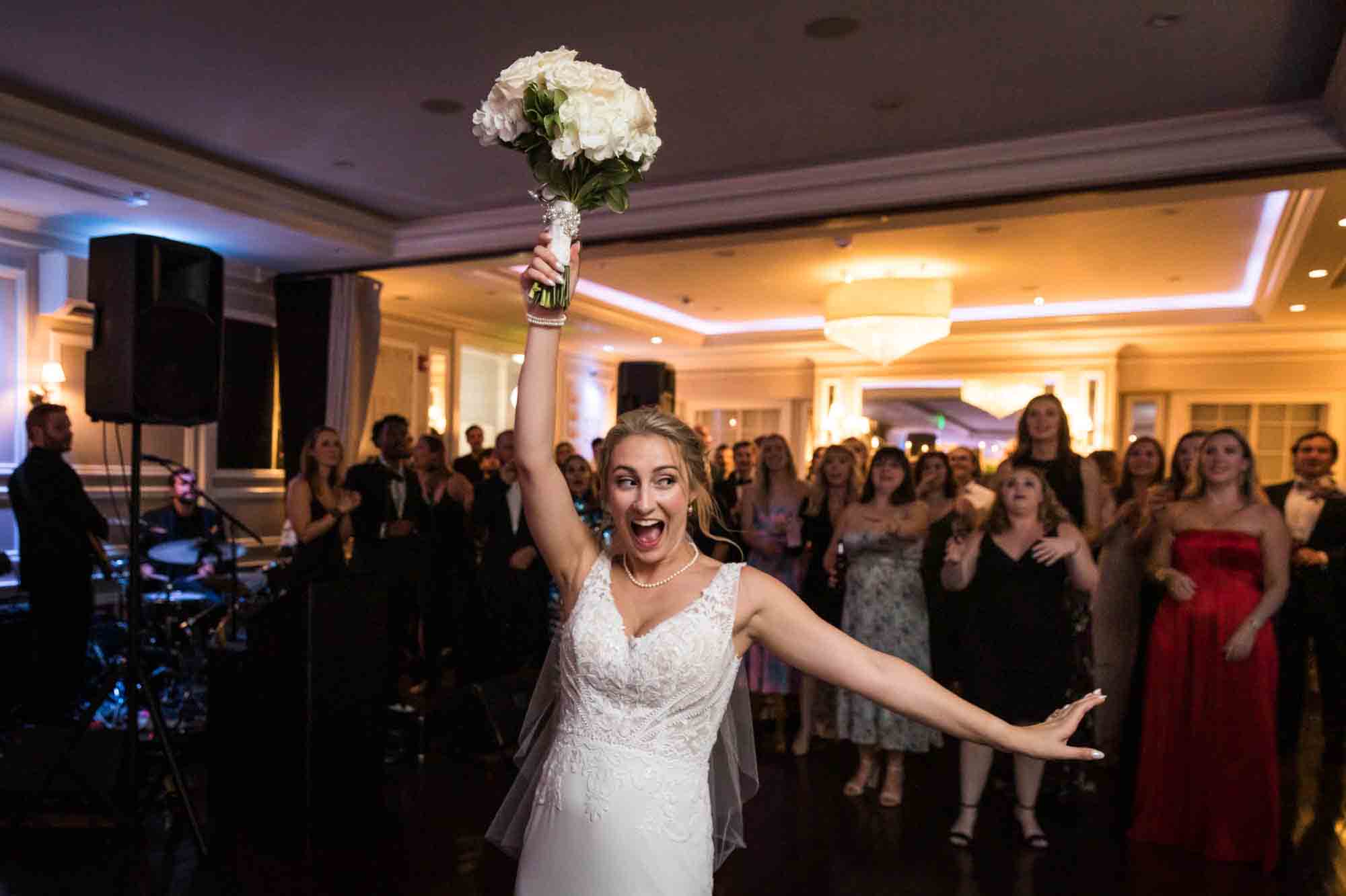 Bride holding white flower bouquet in the air in front of female guests at a Briarcliff Manor wedding