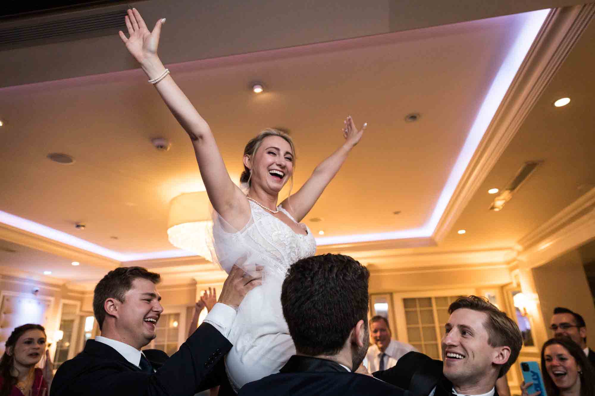 Bride with hands in the air riding on shoulders of guests at a Briarcliff Manor wedding