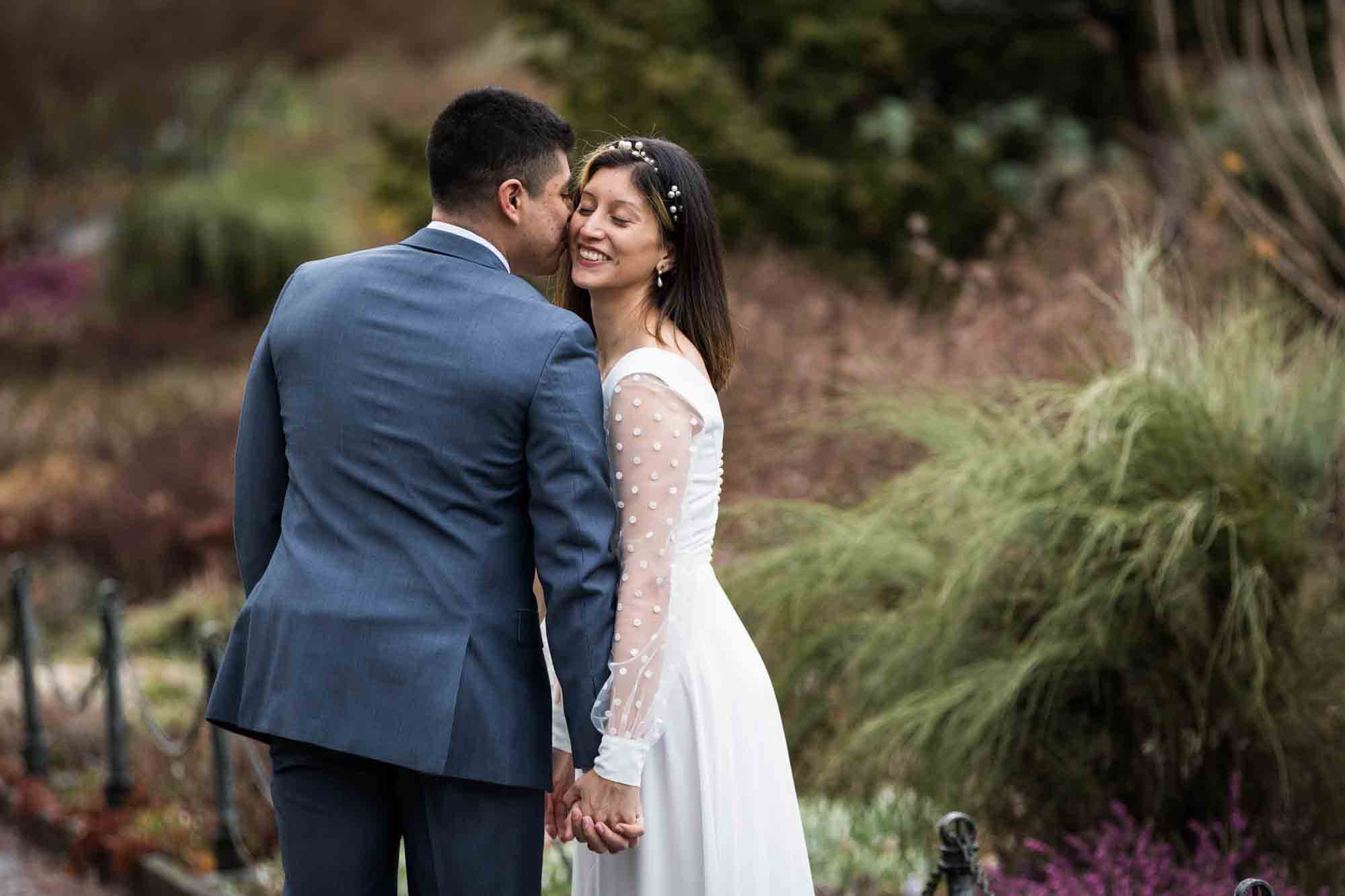 Groom giving kiss to bride on the cheek in Fort Tryon Park Heather Garden