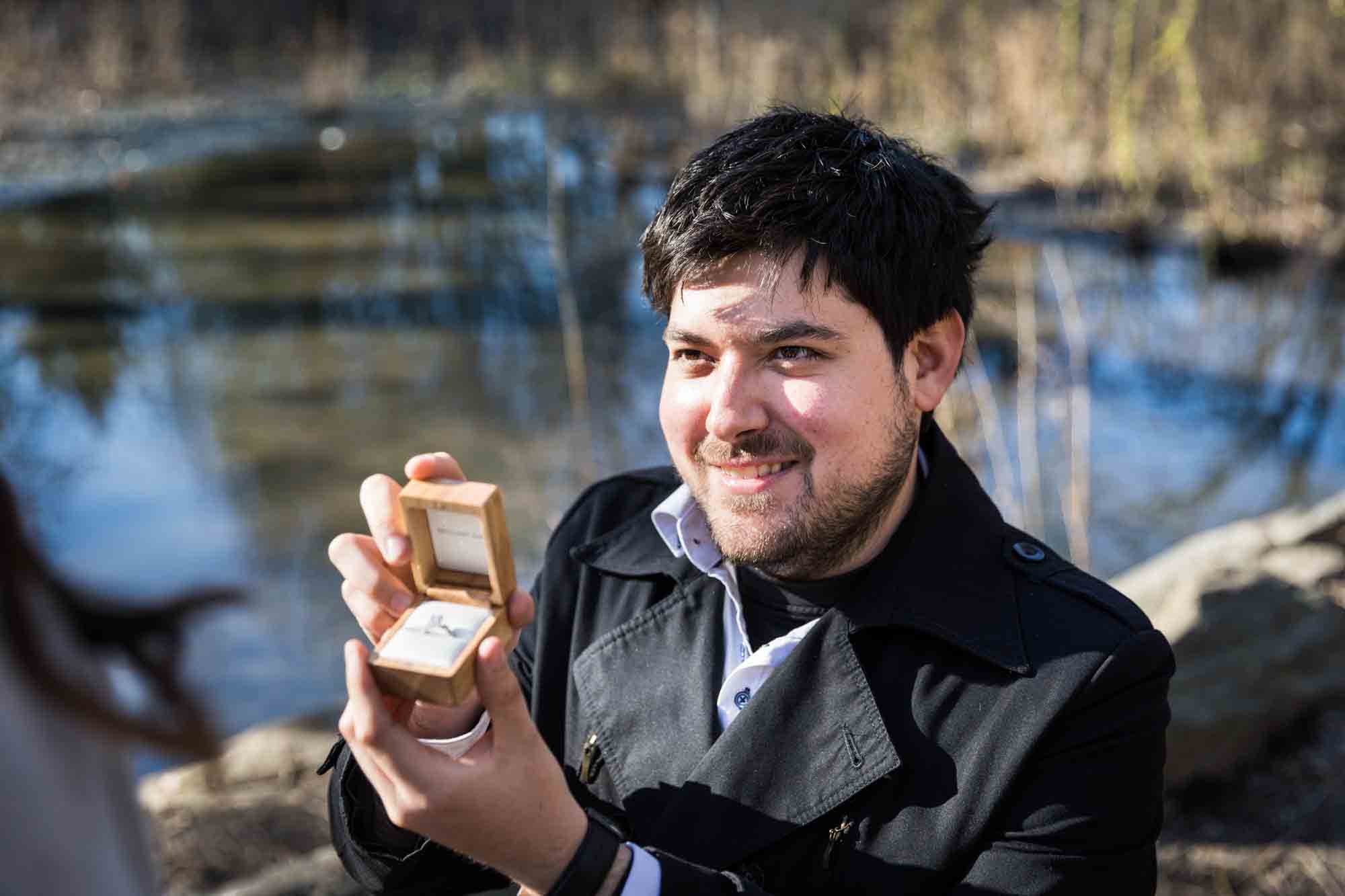 Man holding box with engagement ring during a Gapstow Bridge surprise proposal in Central Park