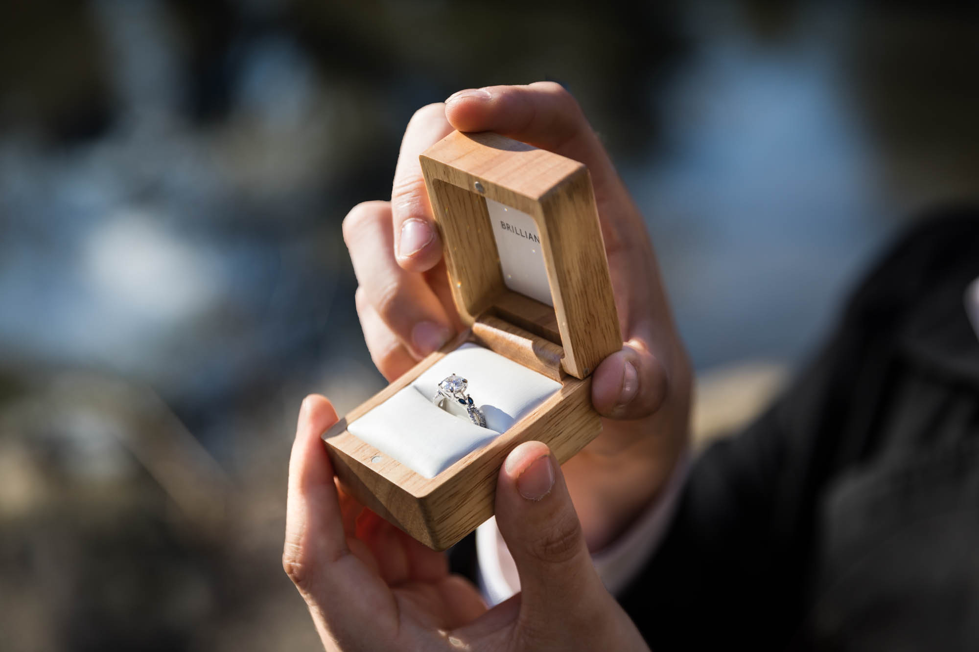 Close up of man's hand holding wooden box with engagement ring during a Gapstow Bridge surprise proposal in Central Park