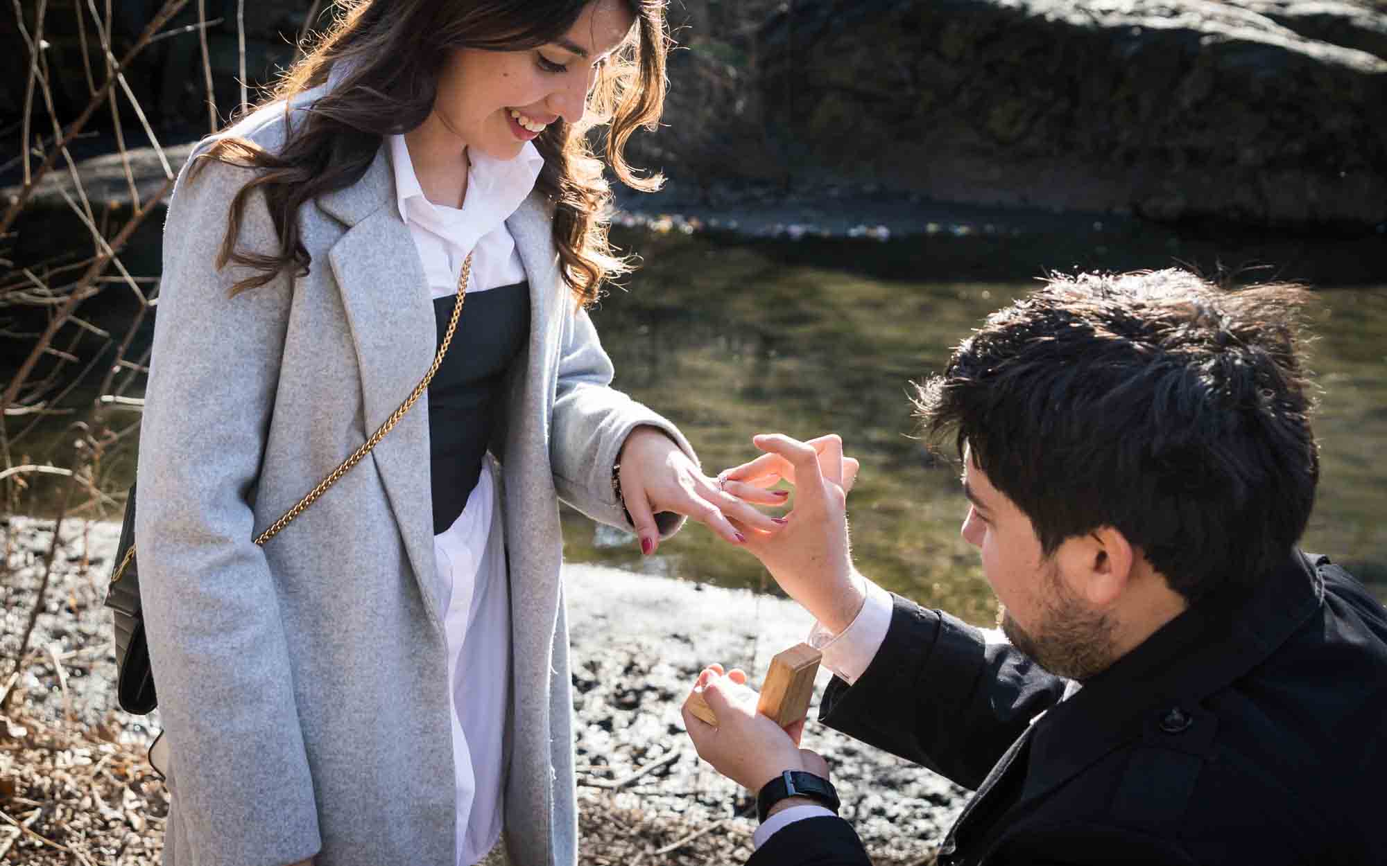 Man putting engagement ring on woman's finger during a Gapstow Bridge surprise proposal in Central Park