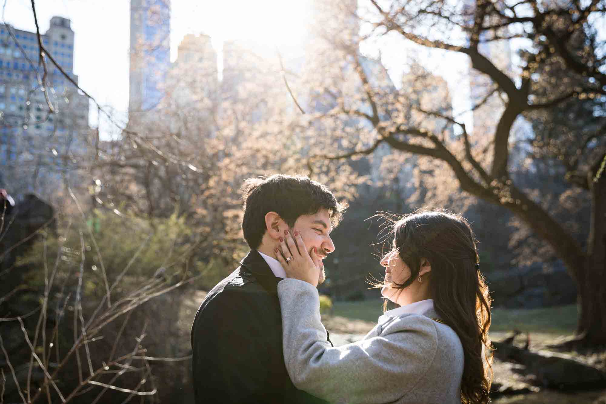 Woman holding man with hand on his cheek during a Gapstow Bridge surprise proposal in Central Park