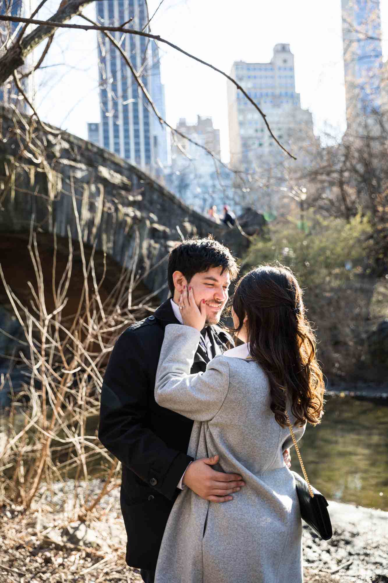 Woman with hand on man's cheek during a Gapstow Bridge surprise proposal in Central Park