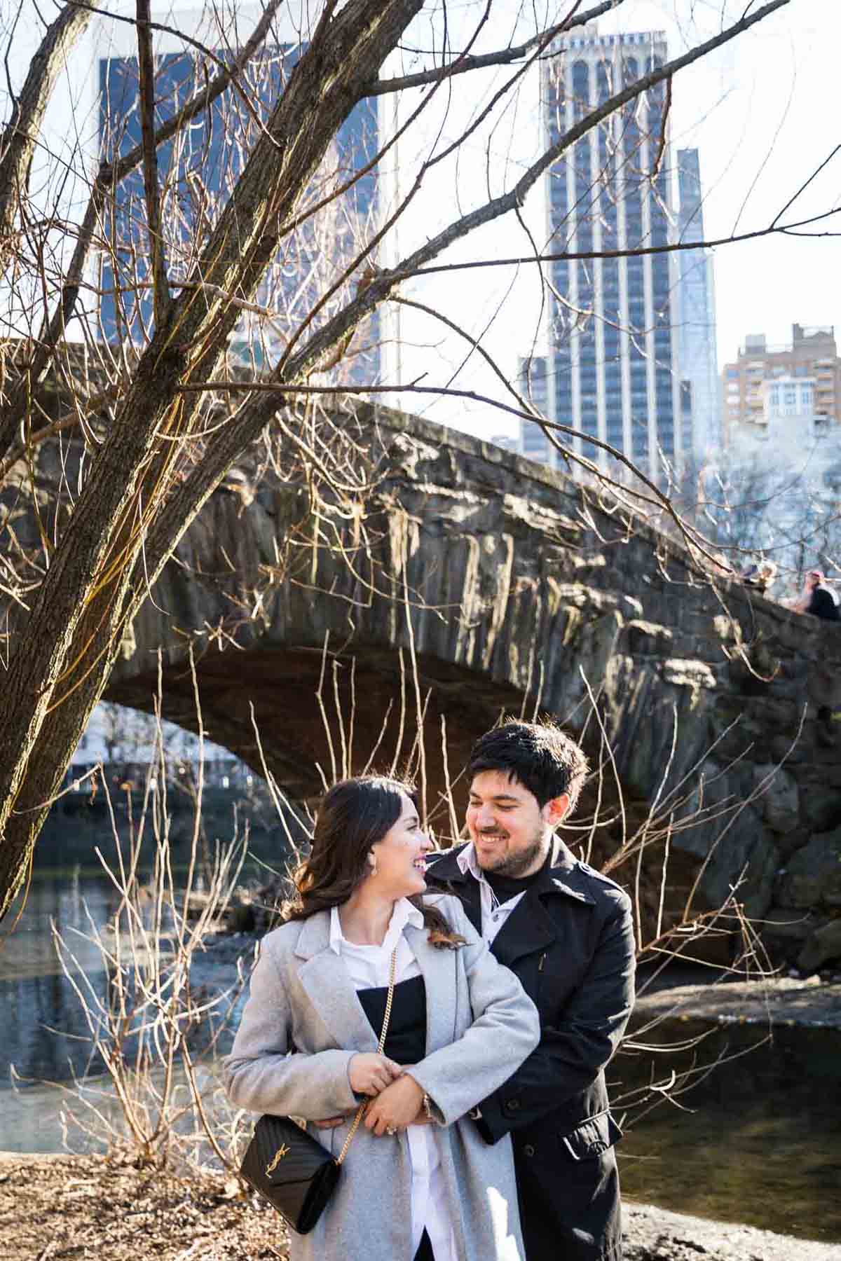 Couple hugging in front of bridge during a Gapstow Bridge surprise proposal in Central Park