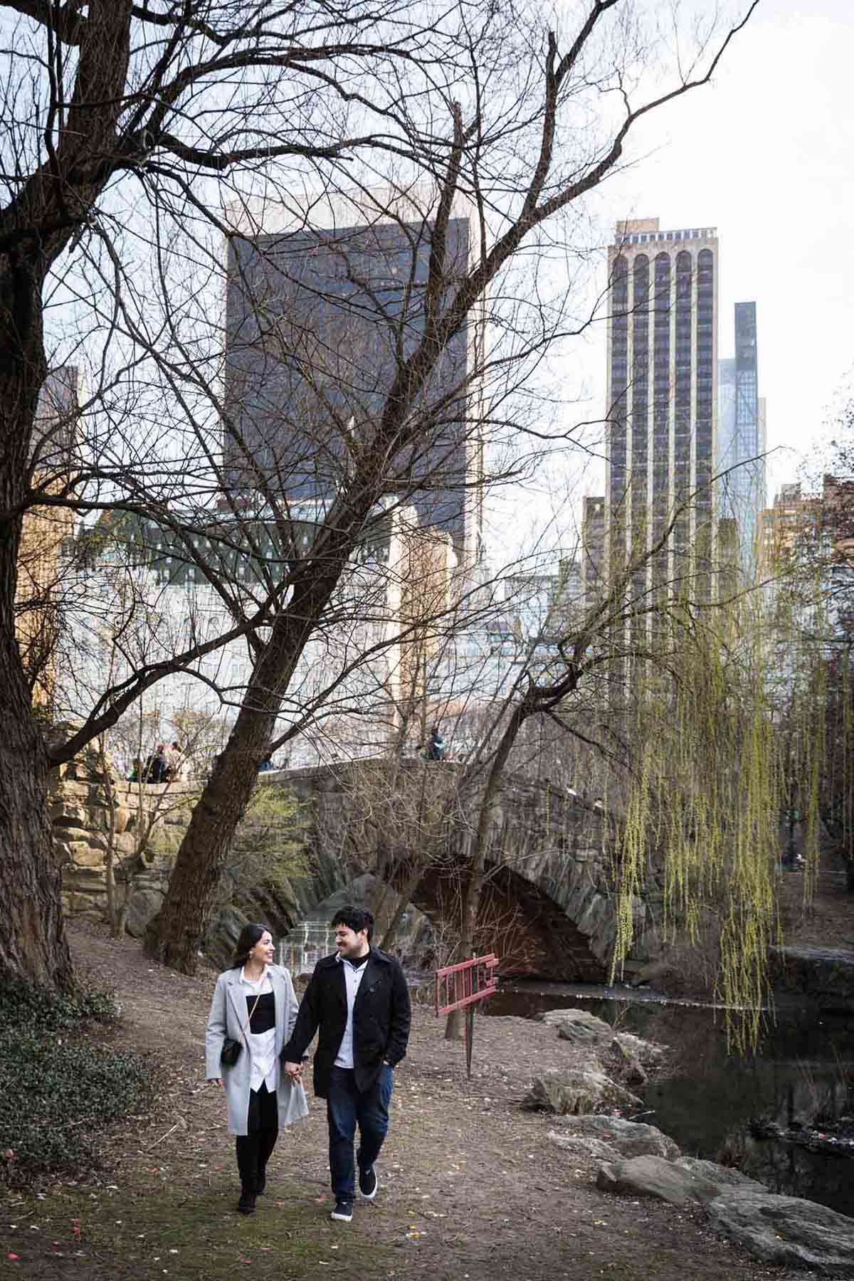 Couple walking in front of Gapstow Bridge and NYC skyline during a Central Park surprise proposal
