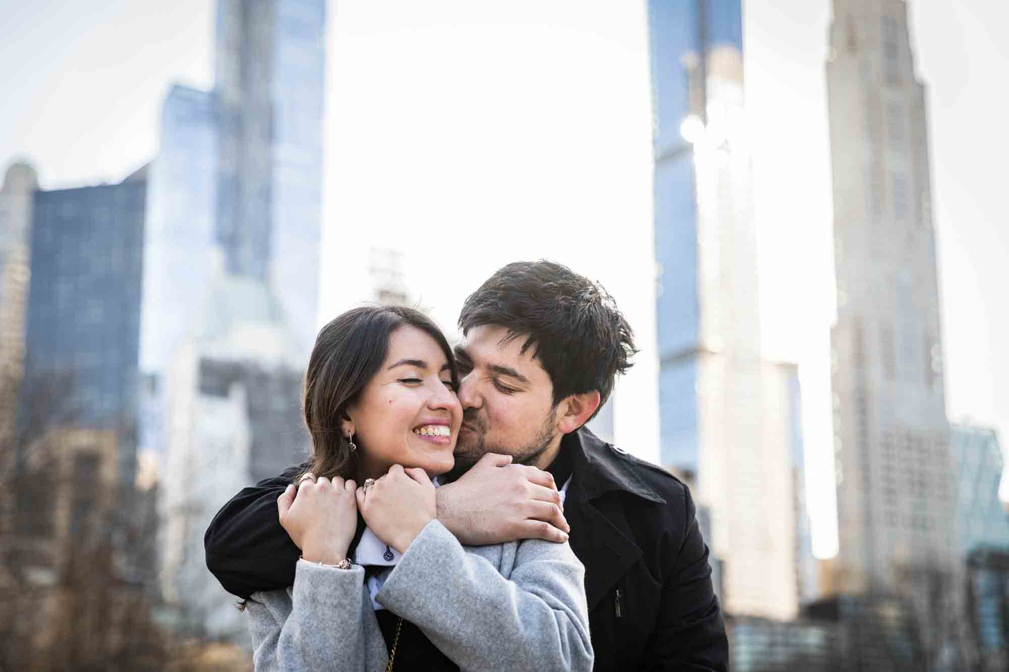 Man kissing woman on the cheek while hugging her shoulders during a Central Park surprise proposal