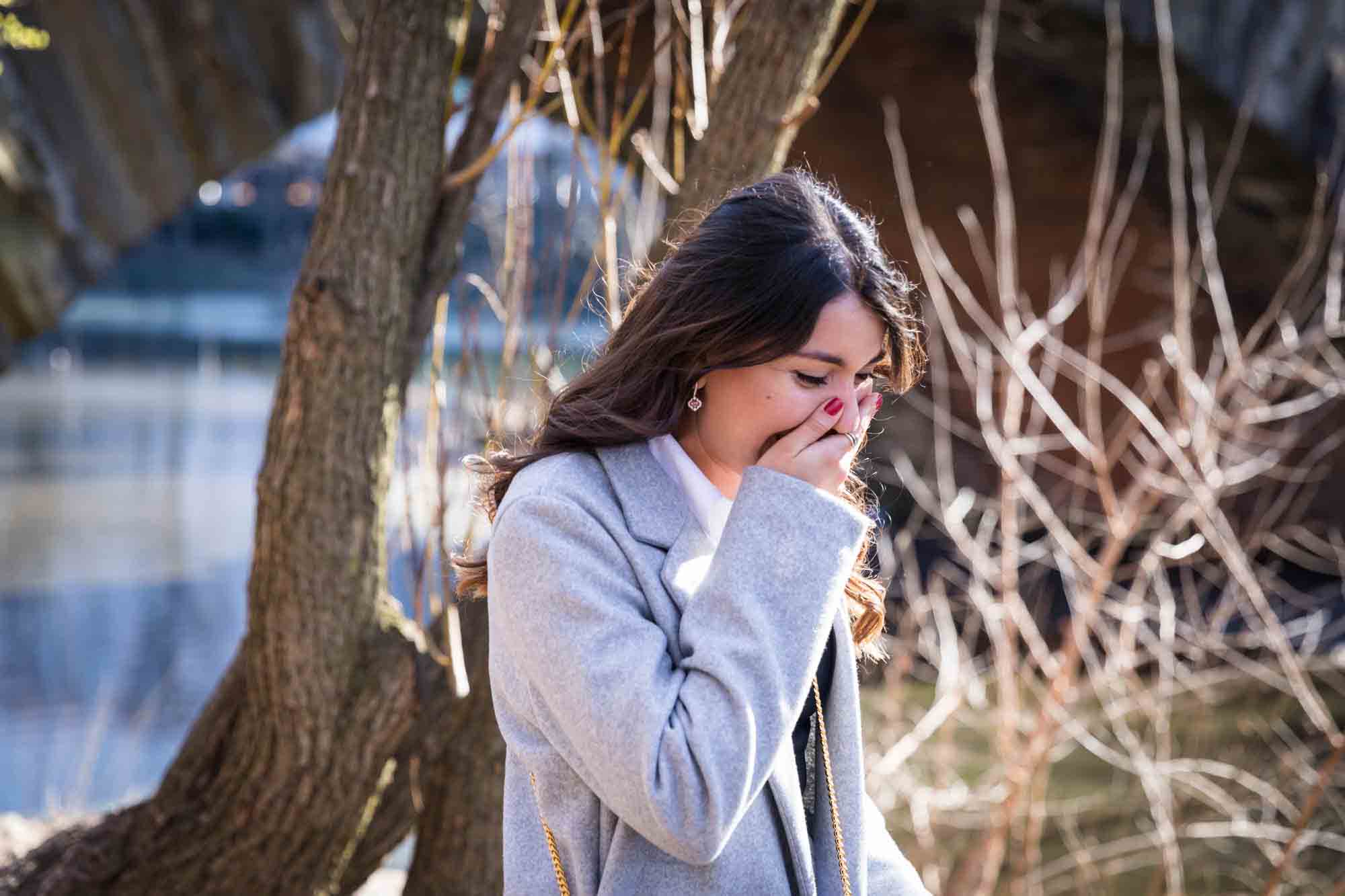 Woman with hand over mouth in surprised expression during a Gapstow Bridge surprise proposal in Central Park