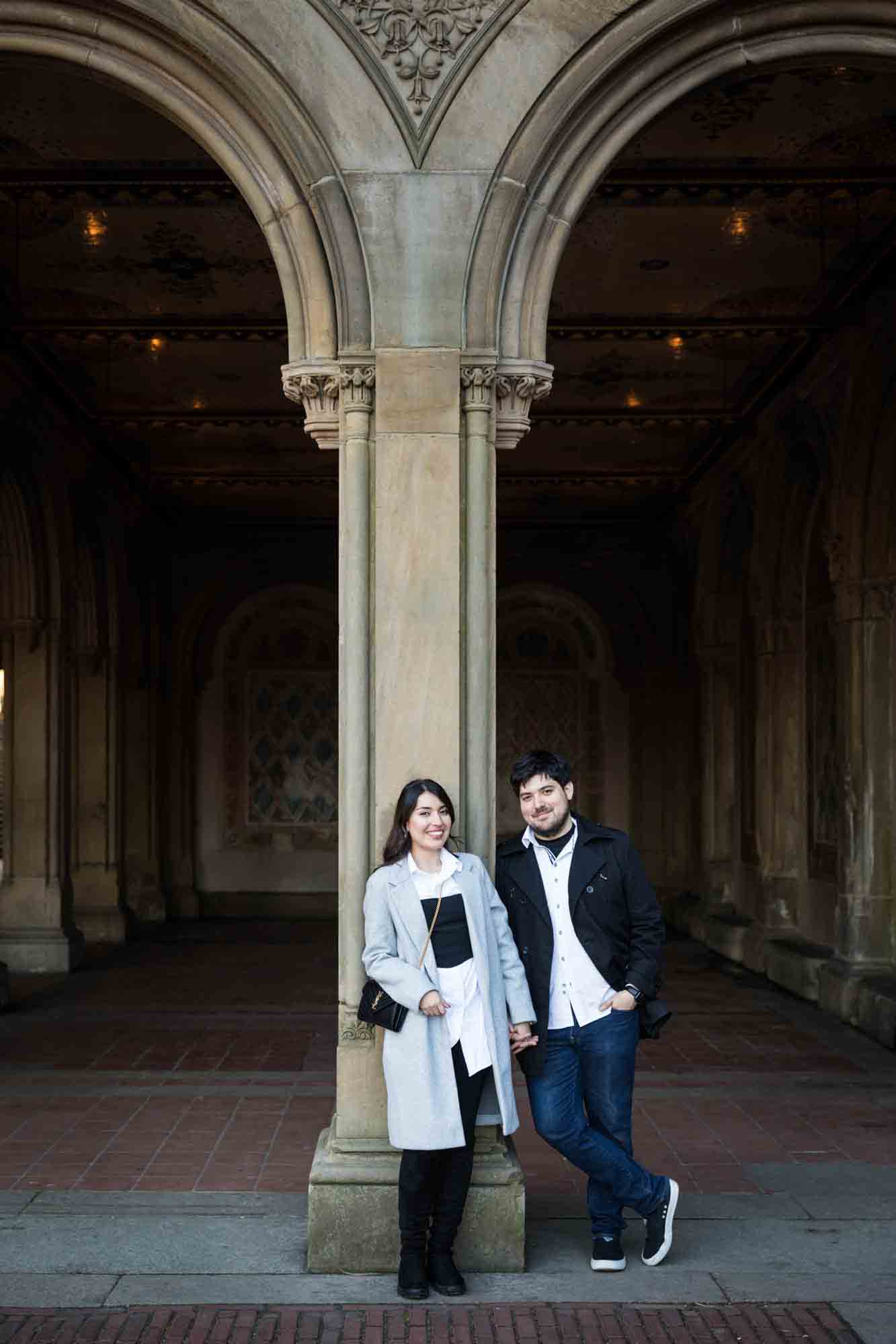 Couple holding hands in front of column in Bethesda Terrace after a NYC surprise proposal