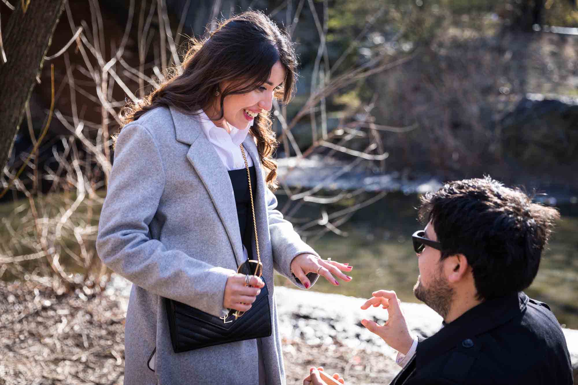 Woman looking down at engagement ring on her hand during a Gapstow Bridge surprise proposal in Central Park