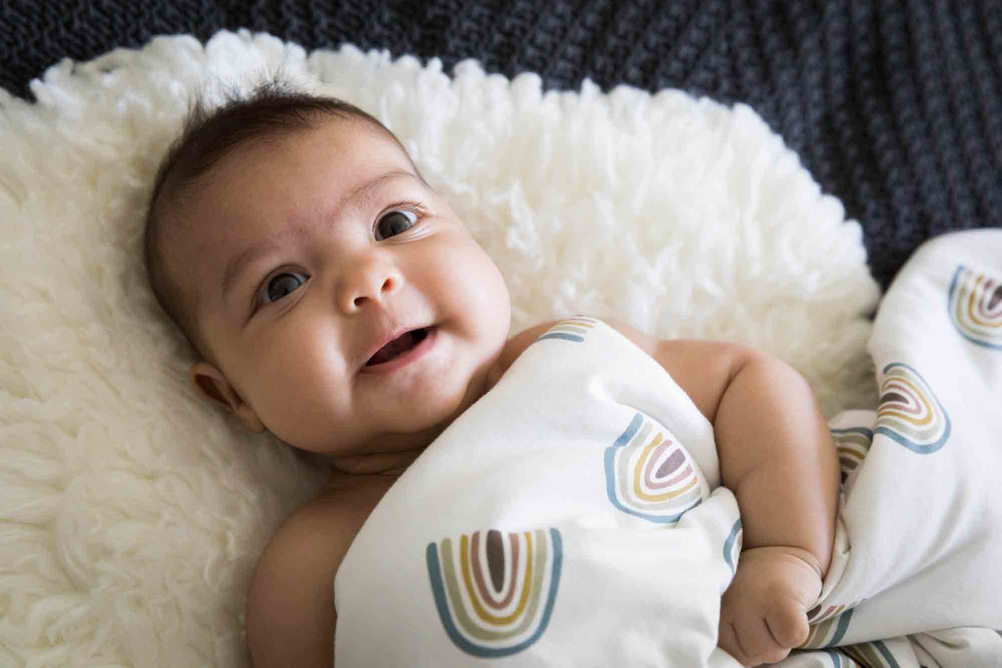 Manhattan family portrait session of smiling baby laying on white rug covered in rainbow blanket