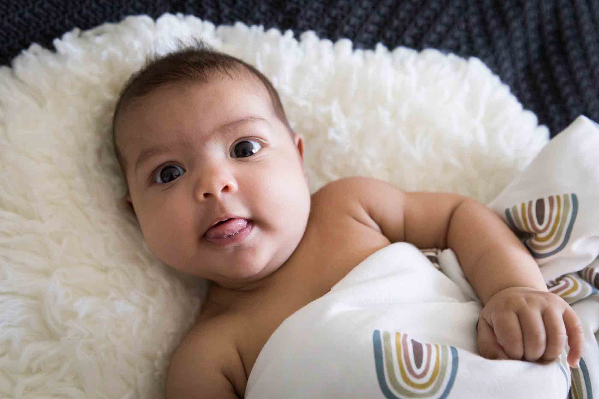 Manhattan family portrait session of smiling baby laying on white rug covered in rainbow blanket