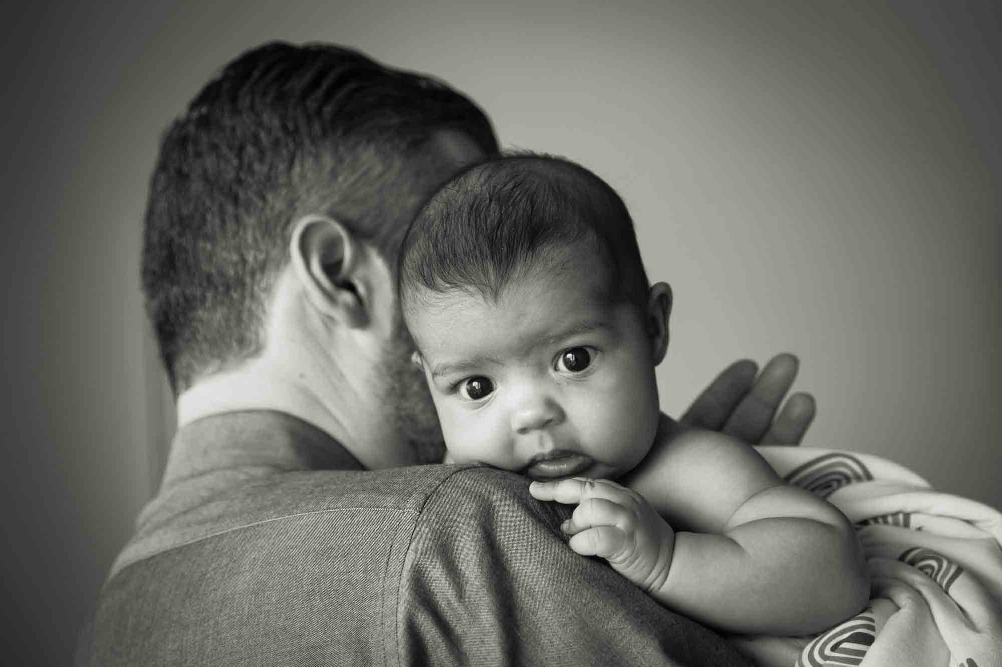 Black and white photo of father holding newborn baby over his shoulder