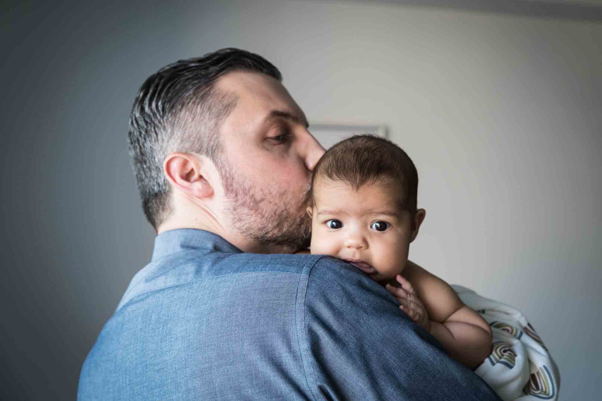 Father holding newborn over his shoulder kissing baby's head