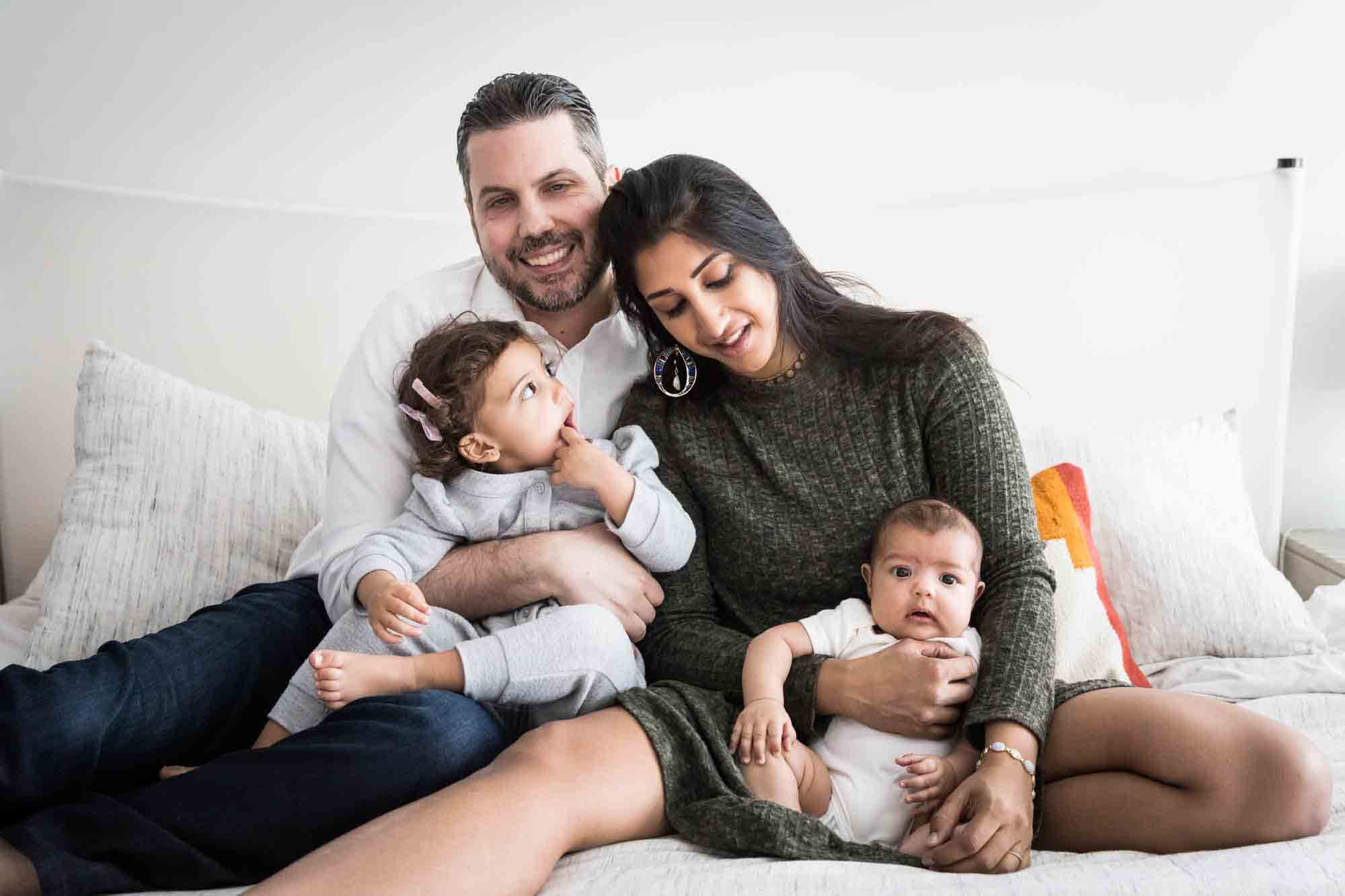 Manhattan family portrait session of parents holding toddler and baby on bed