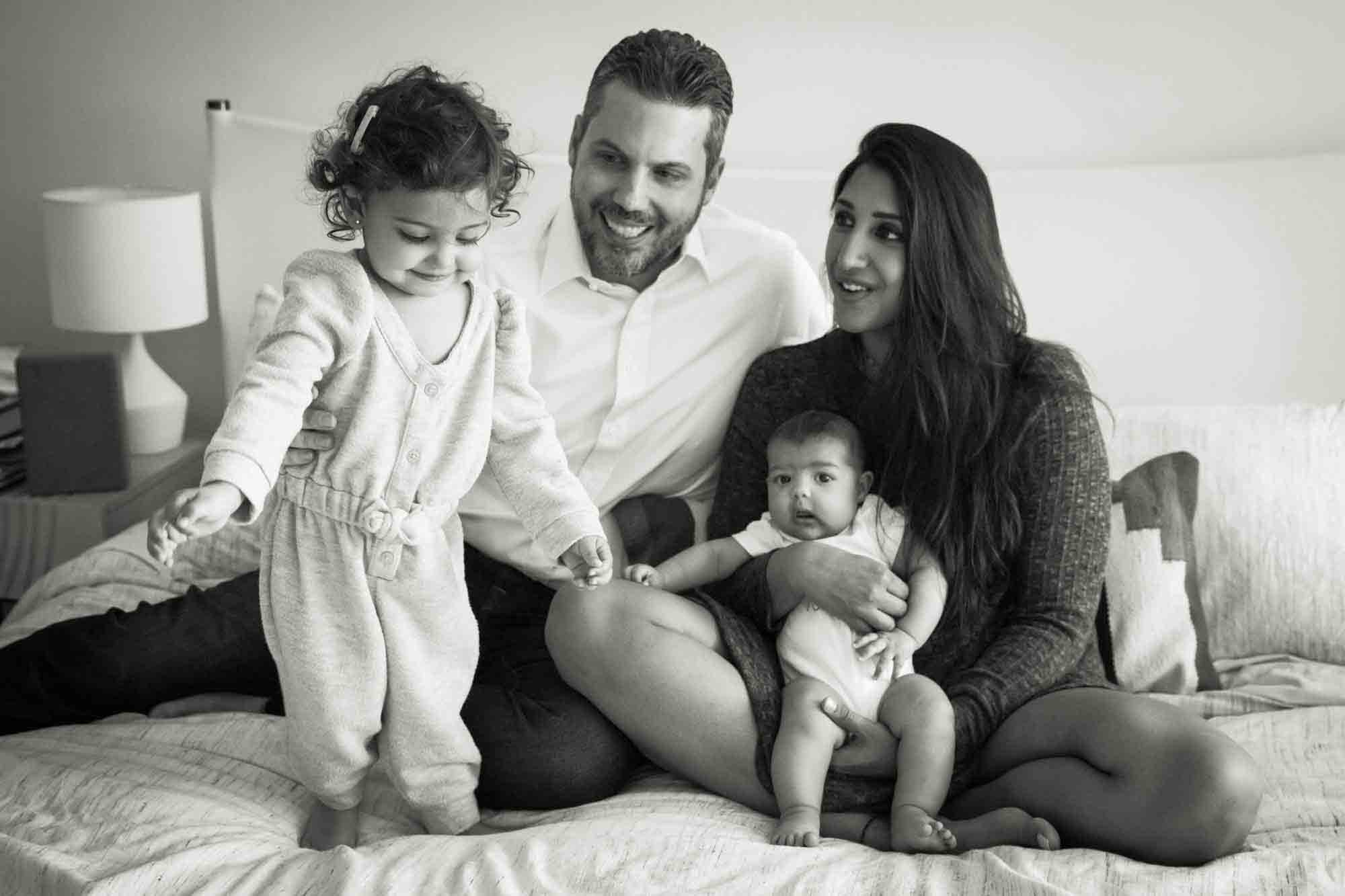 Black and white photo of Manhattan family portrait session of parents playing with toddler and baby on bed