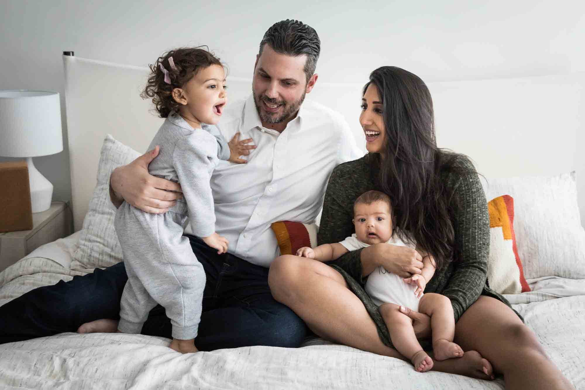 Manhattan family portrait session of parents playing with toddler and baby on bed
