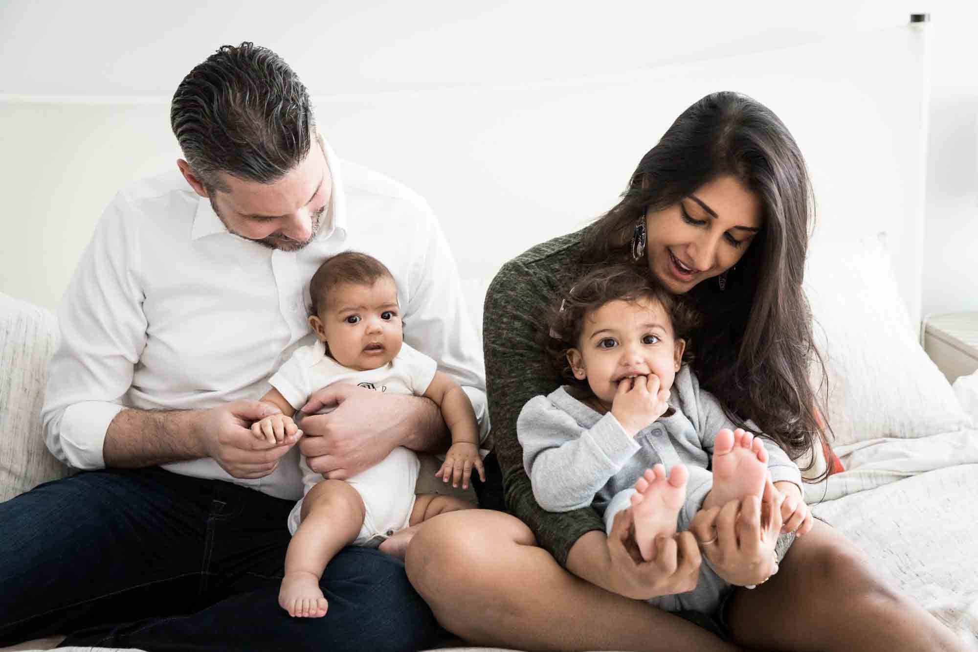 Manhattan family portrait session of parents playing with toddler and baby on bed