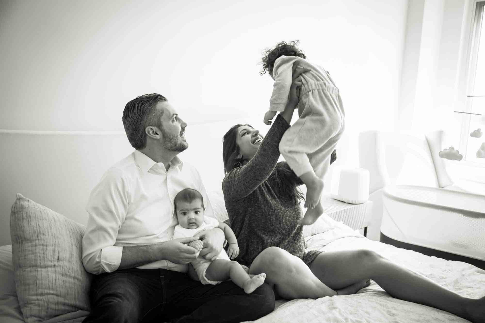 Black and white photo of Manhattan family portrait session of parents playing with toddler and baby on bed