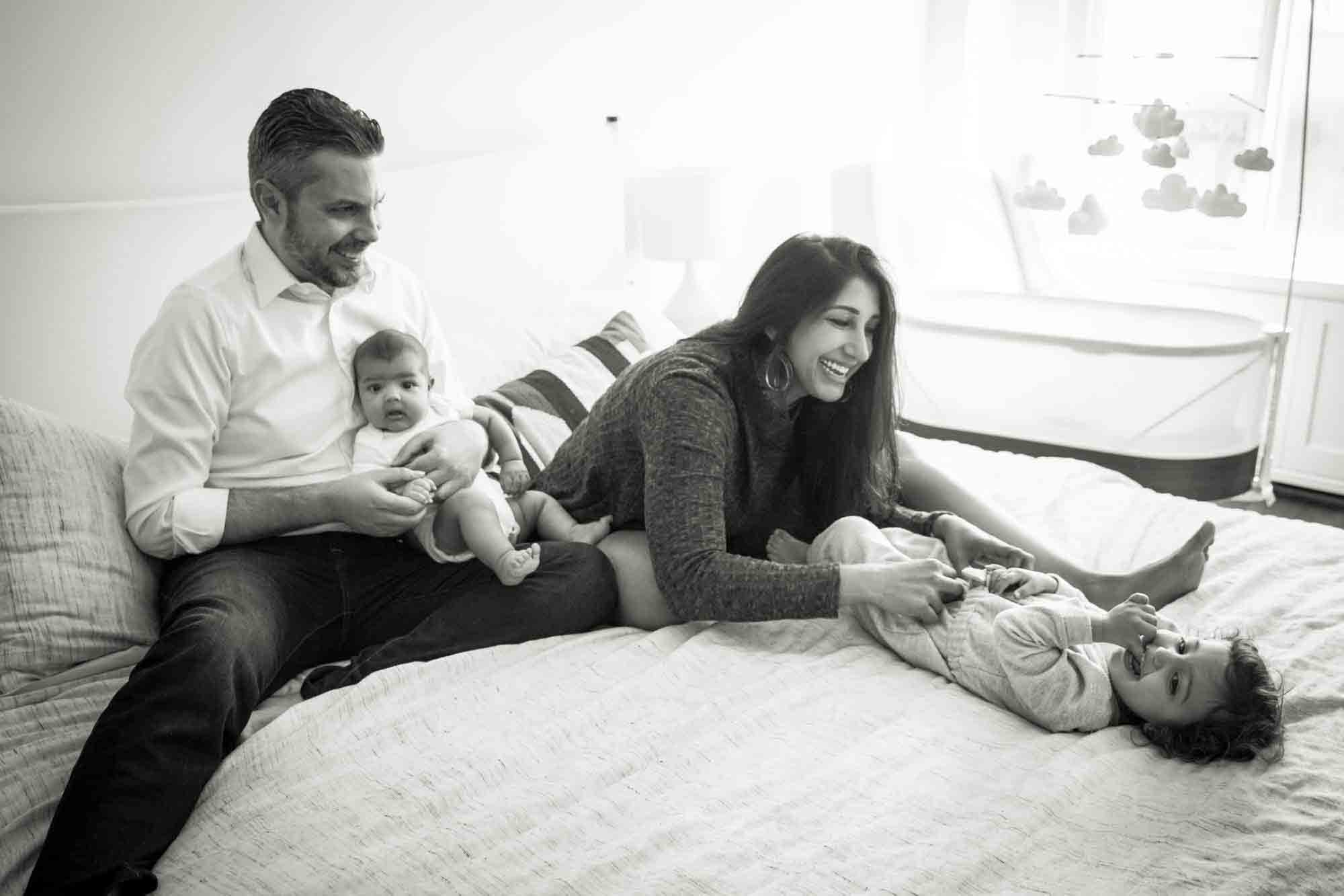 Black and white photo of Manhattan family portrait session of parents playing with toddler and baby on bed