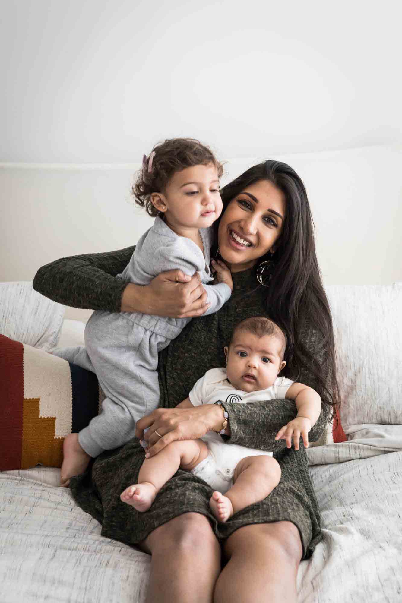 Mother playing with little girl and baby on bed during a NYC family portrait session