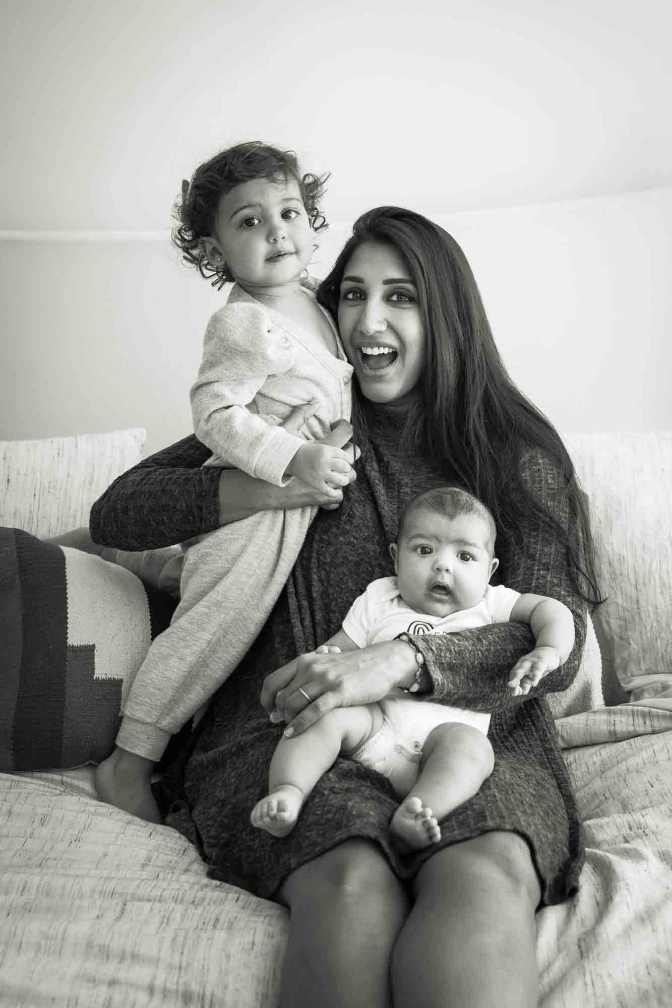 Black and white photo of mother playing with little girl and baby on bed during a NYC family portrait session